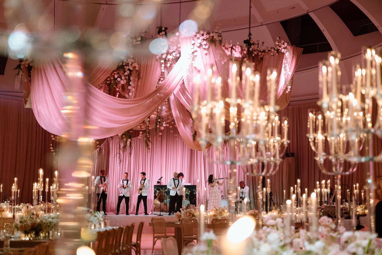 Glamorous wedding venue with crystal chandeliers and pink drapery creating an ethereal ceiling design.
