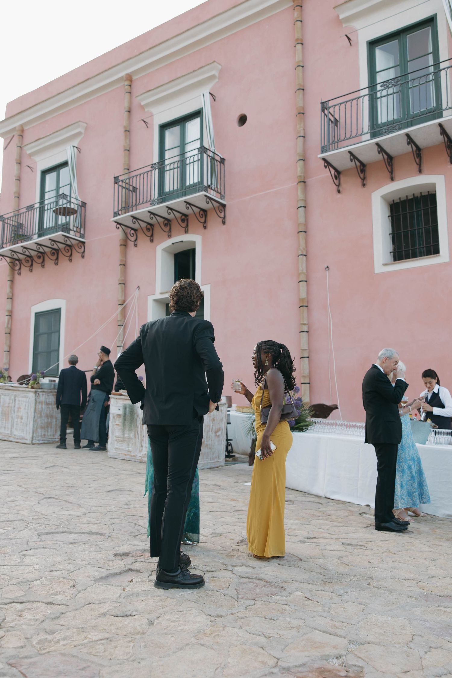 Formal gathering outside pink building with traditional Mediterranean architecture.