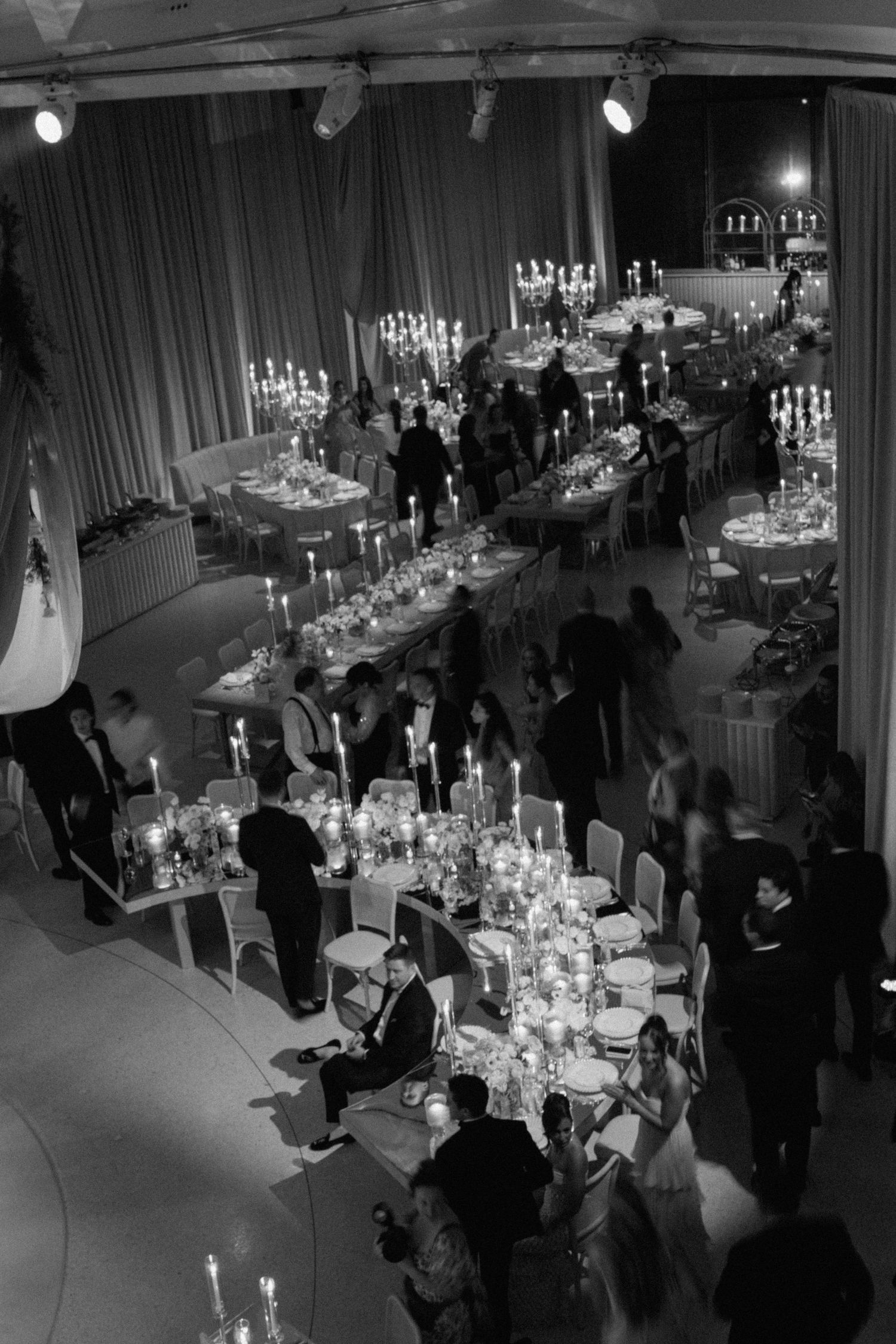 Aerial view of a dimly lit reception venue with guests mingling around decorated tables.