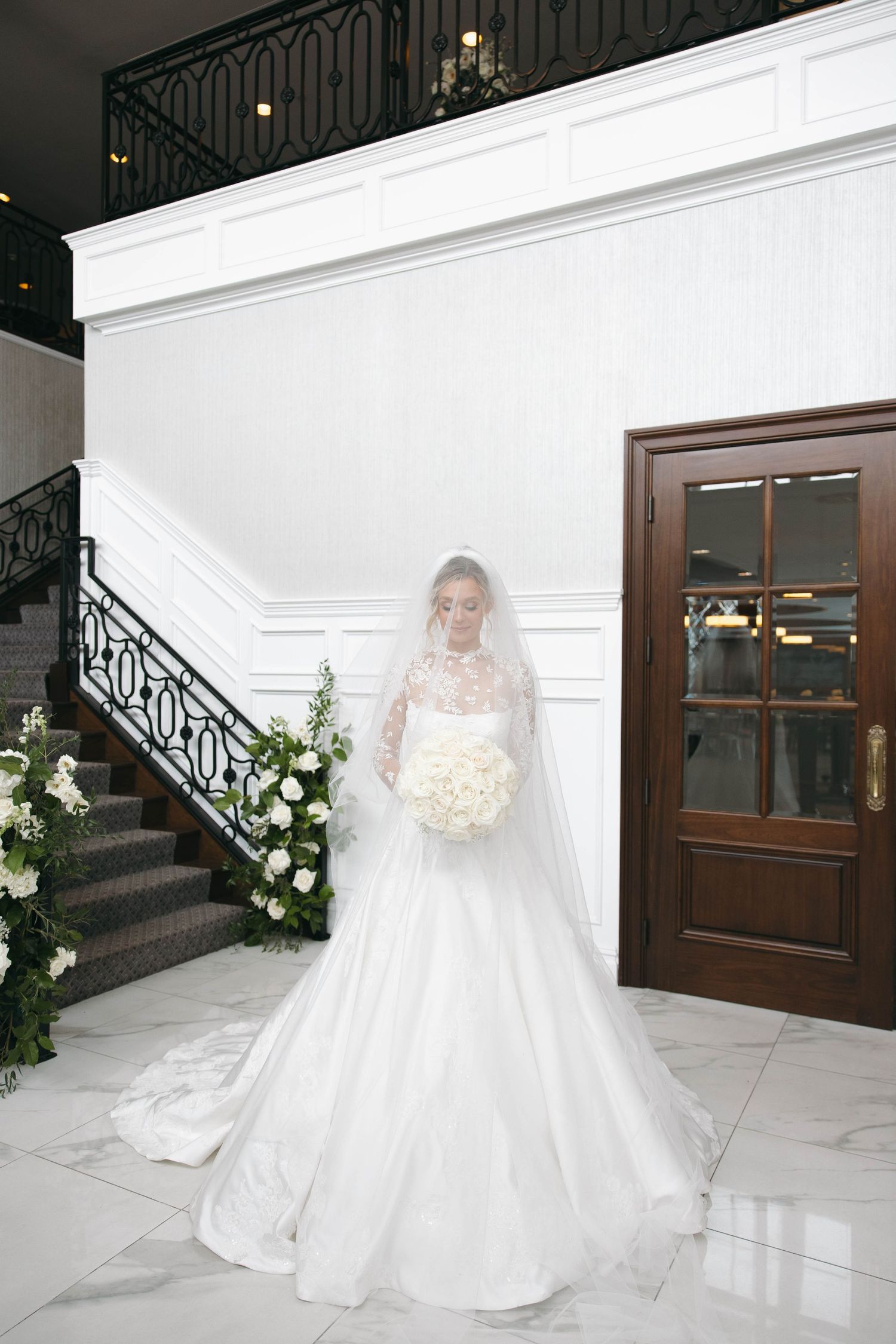 A bride in a flowing white gown walks through an elegant venue with wrought iron details.