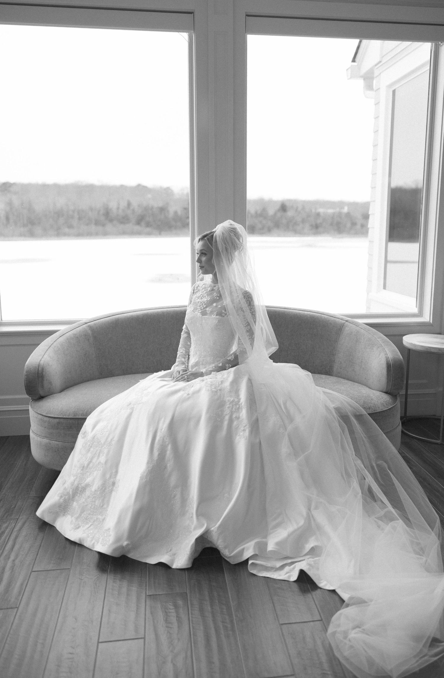 Elegant white wedding dress with flowing train displayed on hardwood floor in natural window light.