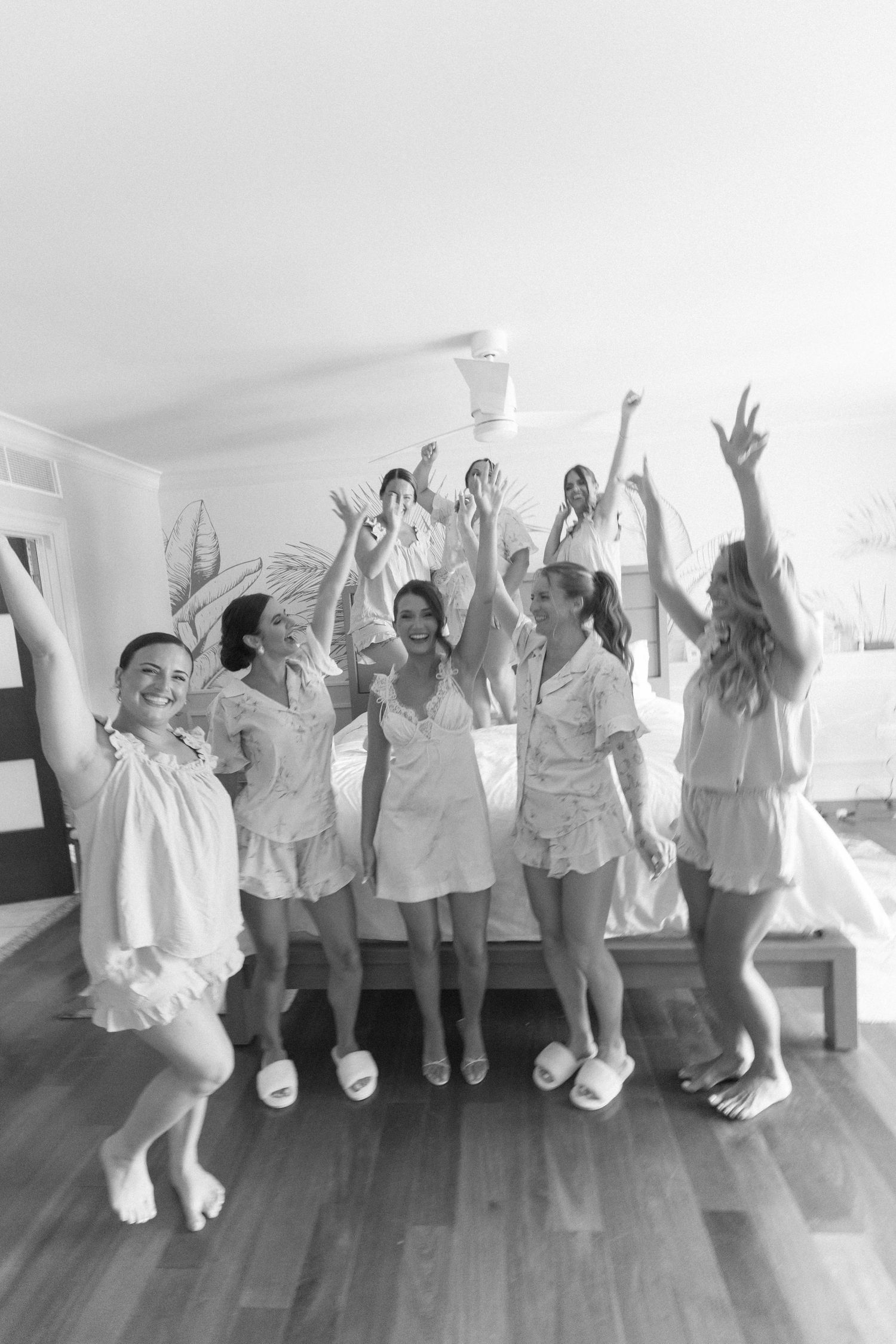 Black and white photo of bridesmaids in matching pajamas celebrating together in a bedroom.