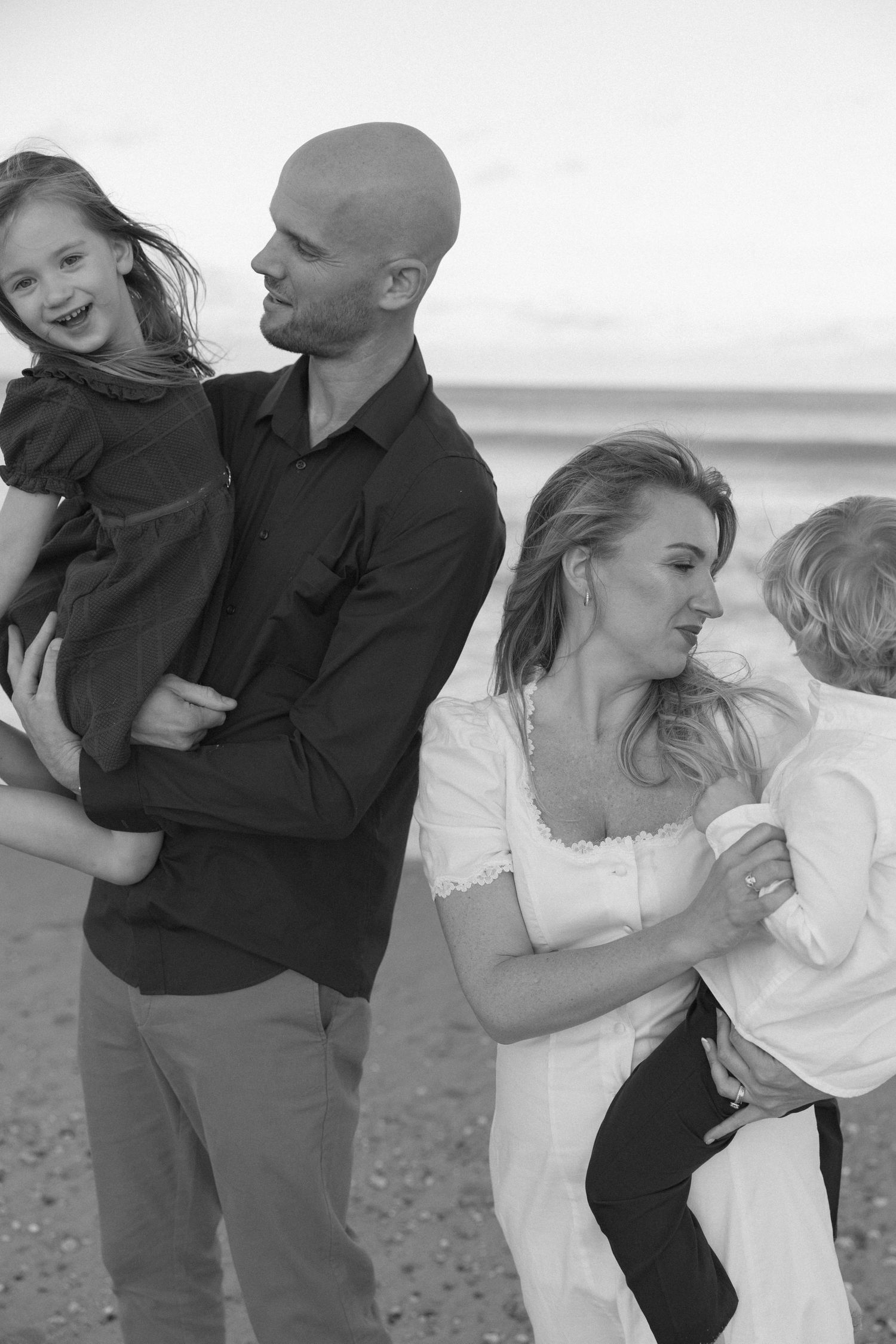 Black and white portrait of a family sharing joyful moments together on the beach.