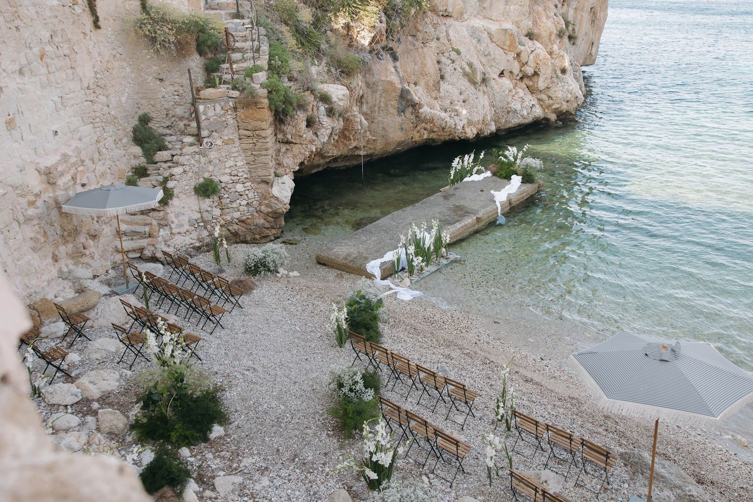 Beachfront wedding setup nestled between limestone cliffs with wooden chairs facing the sea.