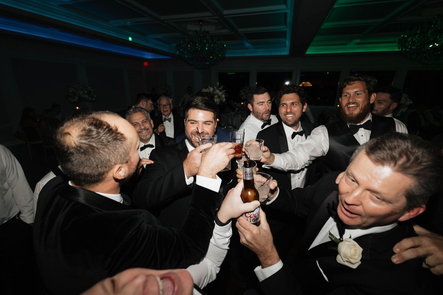 Crowded dance floor at formal event with guests in black tie attire under mood lighting.
