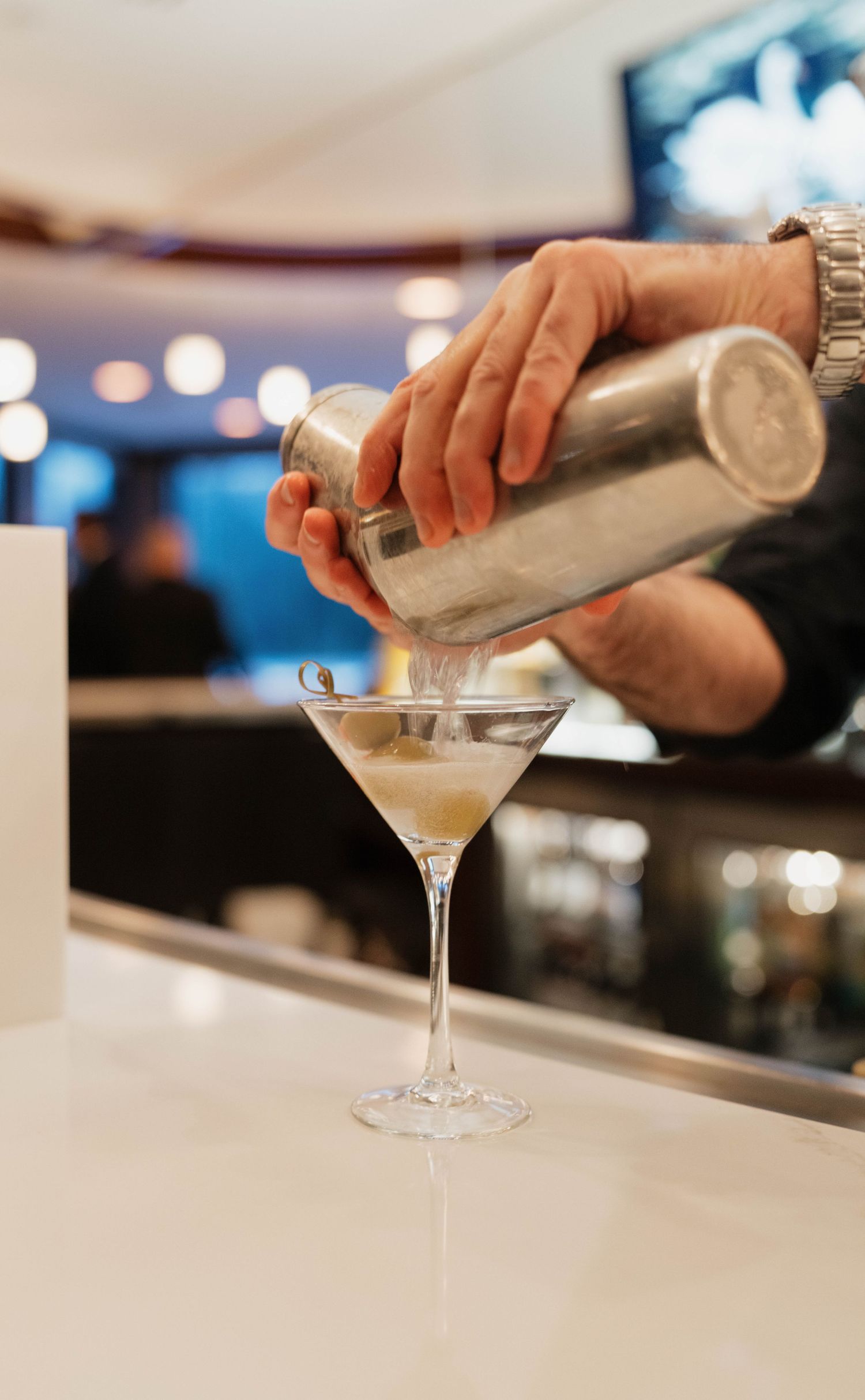 Bartender pouring a martini cocktail into a glass with a shaker.
