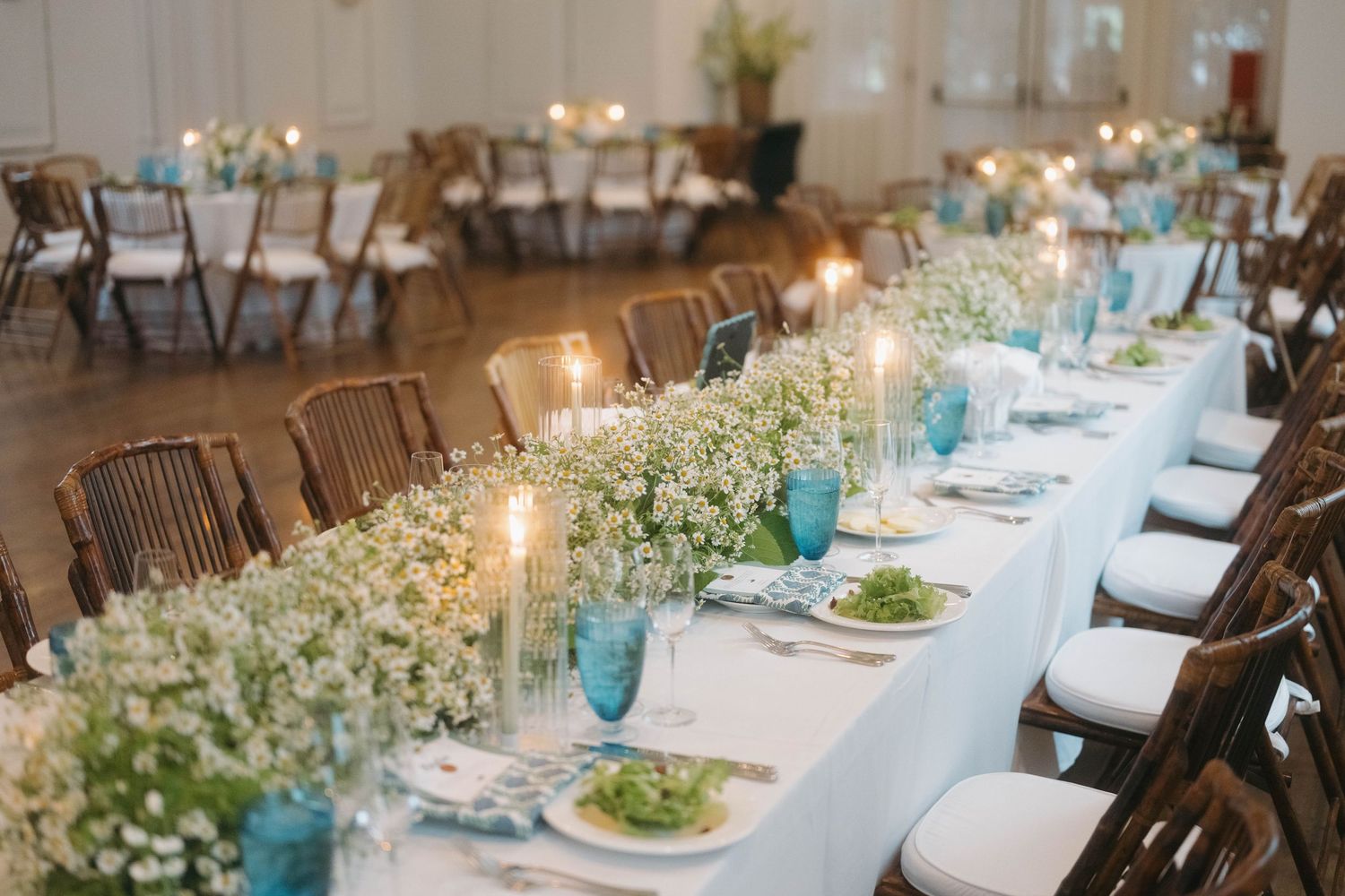Wedding reception tables decorated with white linens and floral centerpieces in a bright venue.