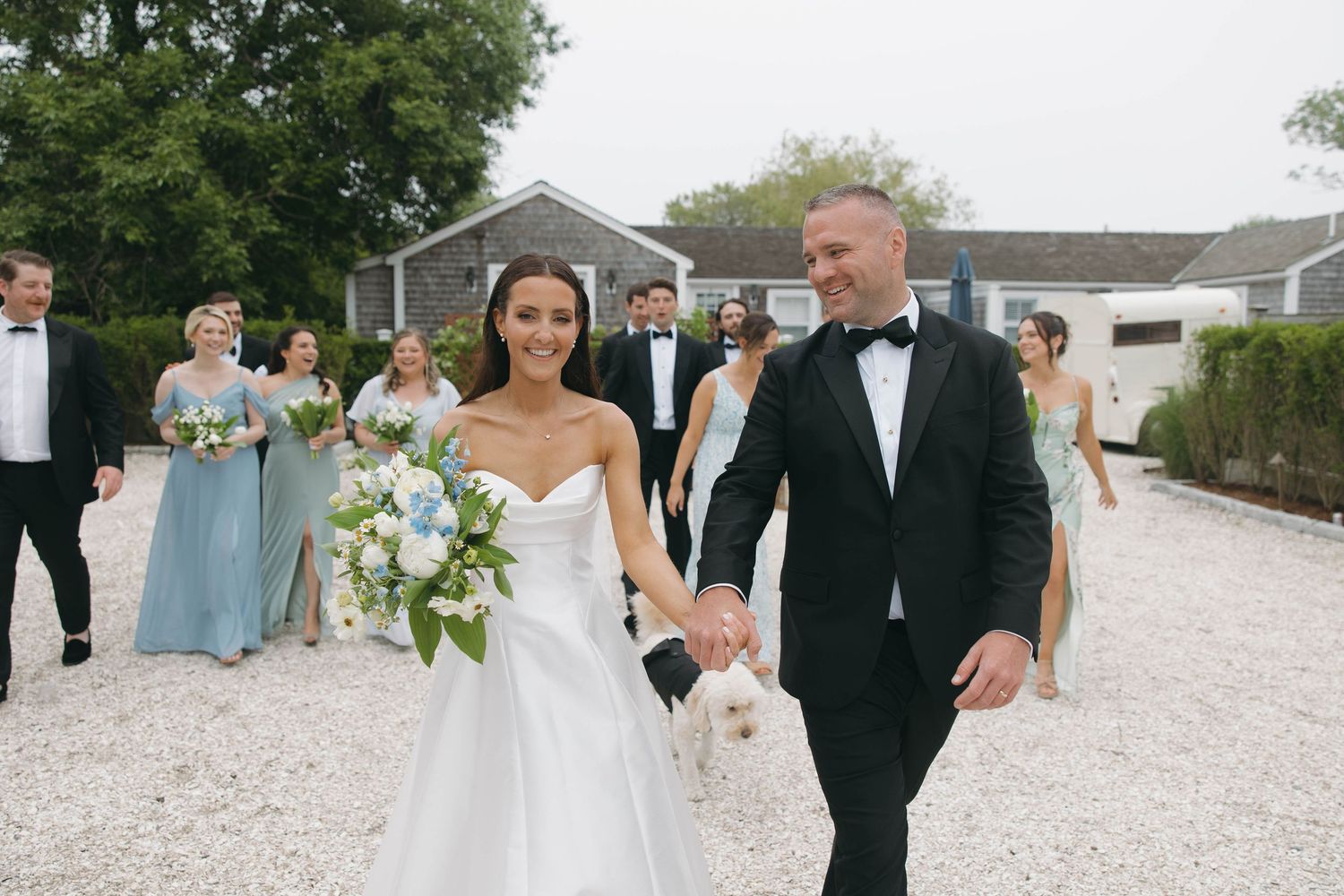Wedding party celebrates joyfully on gravel courtyard in formal attire.