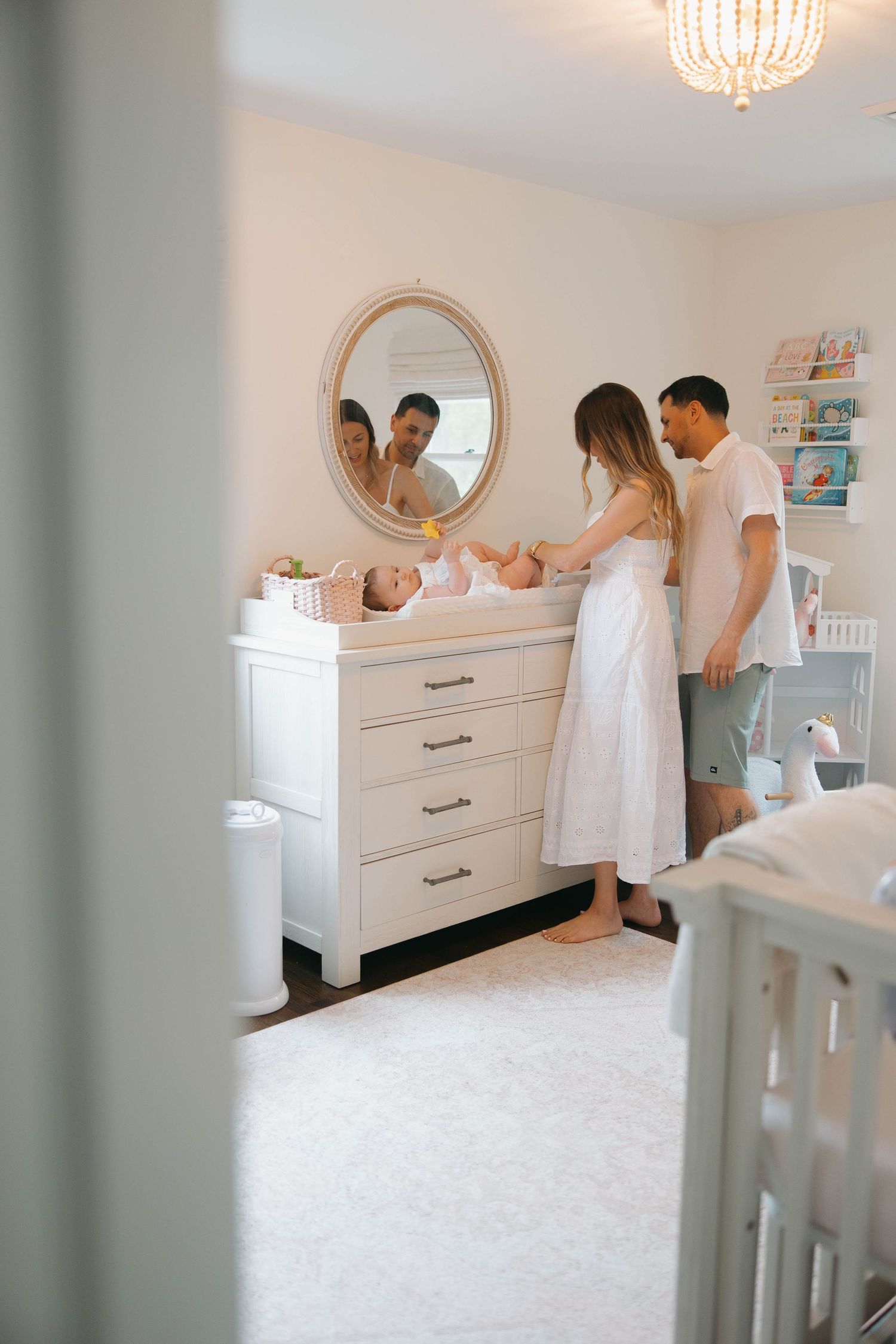 A white dresser being installed against a wall in a bright room with a crystal chandelier and circular mirror.