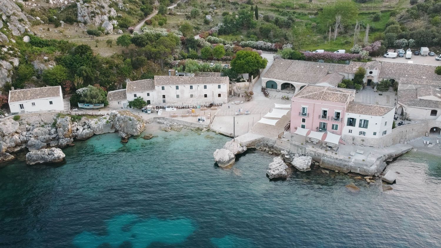 Aerial panorama of Mediterranean seaside village with white buildings and turquoise waters.