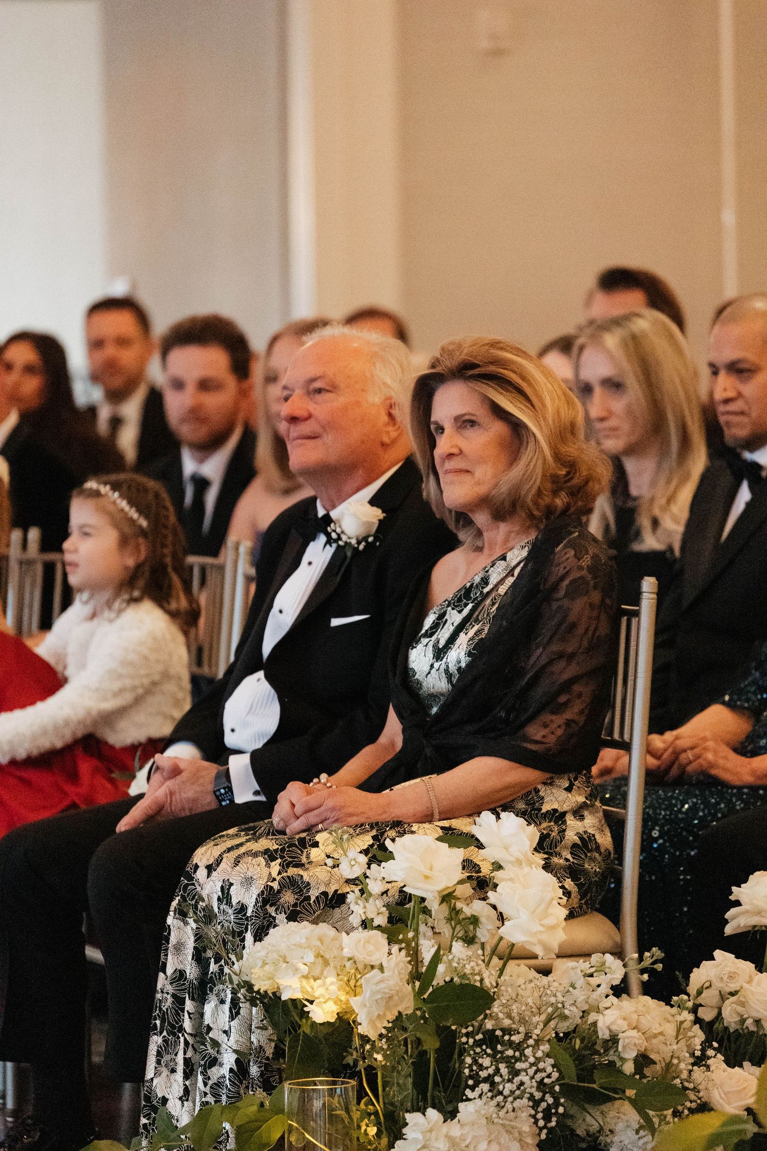 Formal wedding ceremony with guests seated alongside white floral arrangements and candles.