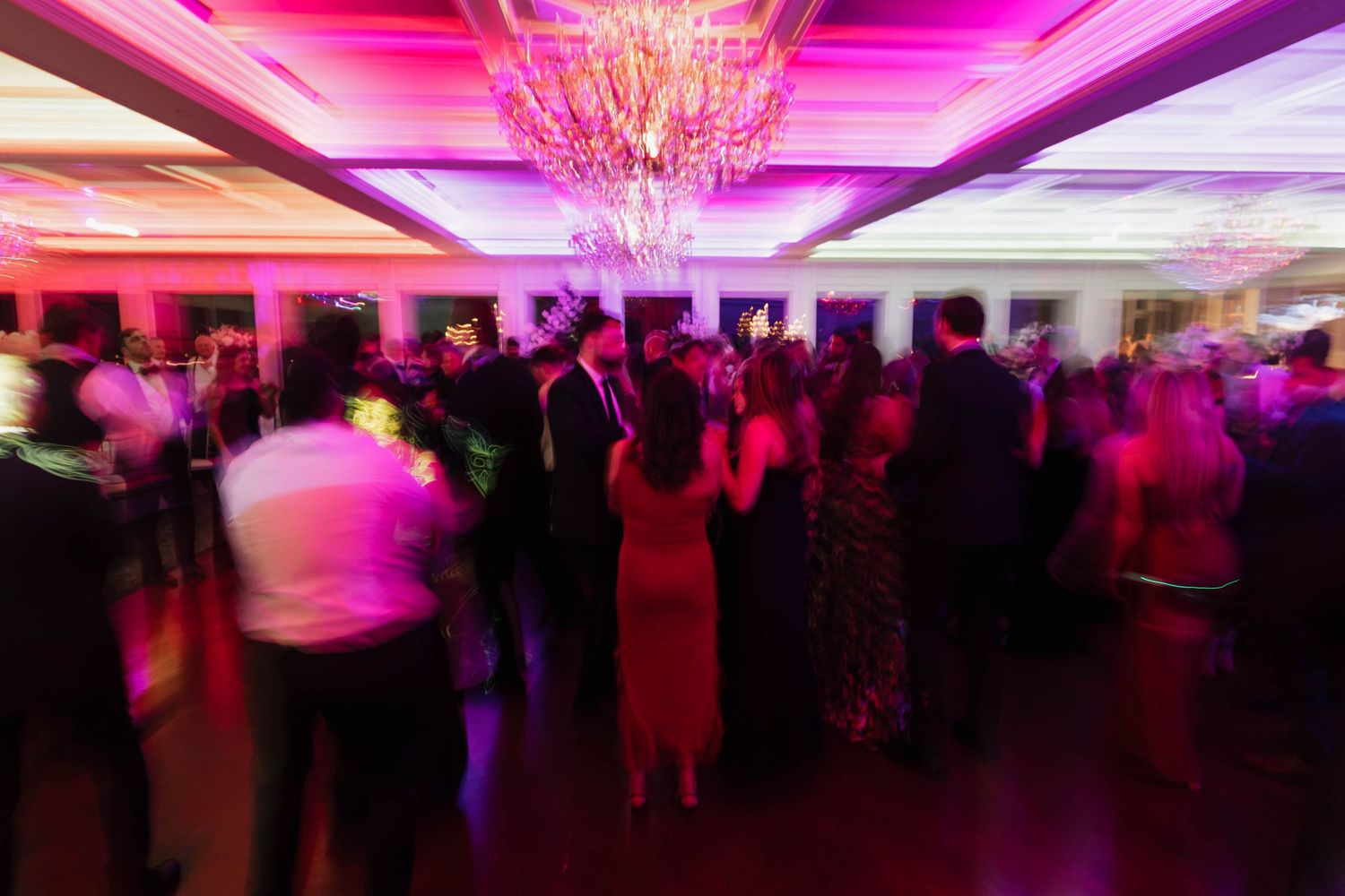 Wedding reception ballroom illuminated with vibrant pink lighting and crystal chandeliers.