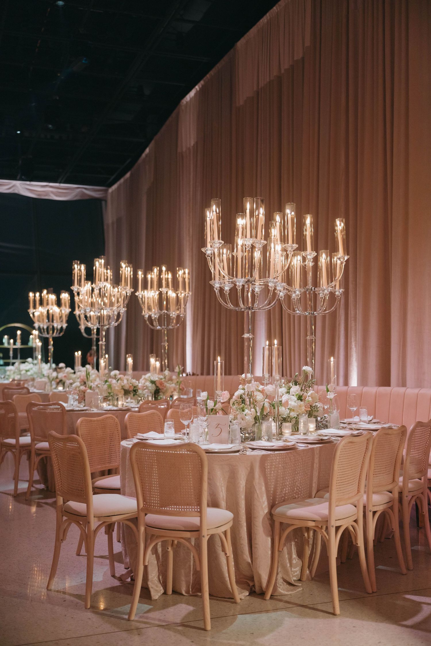 Elegant reception venue with tall crystal candelabras and light wood chairs creating a warm ambiance.
