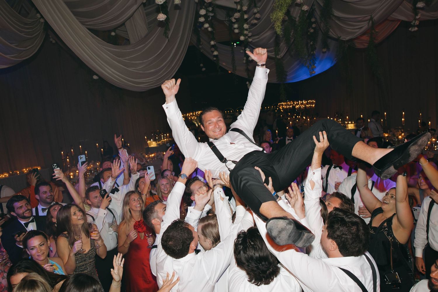 Crowded wedding reception dance floor with guests celebrating under dramatic lighting.