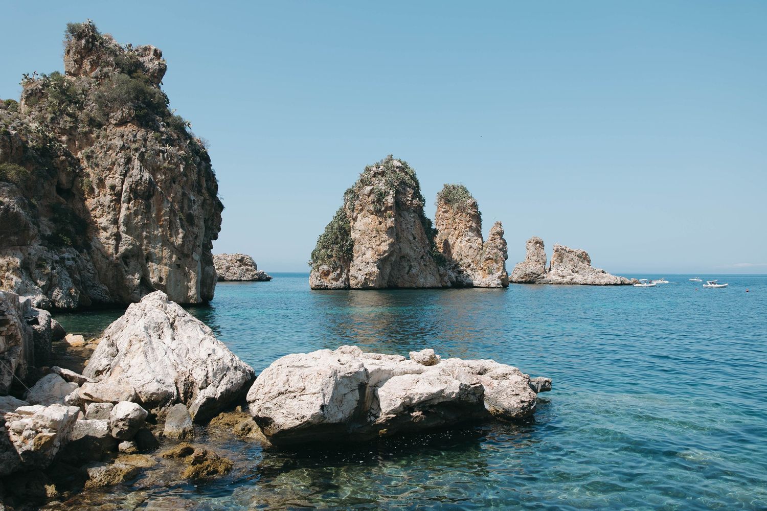Rocky coastal formations and blue waters of the Mediterranean Sea under clear skies.