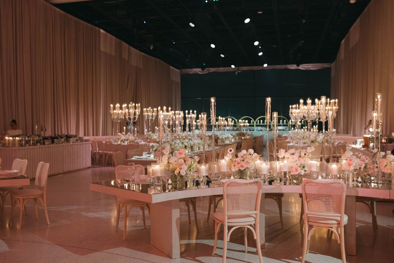 Spacious ballroom set up for a wedding reception with elegant table arrangements and dramatic lighting.