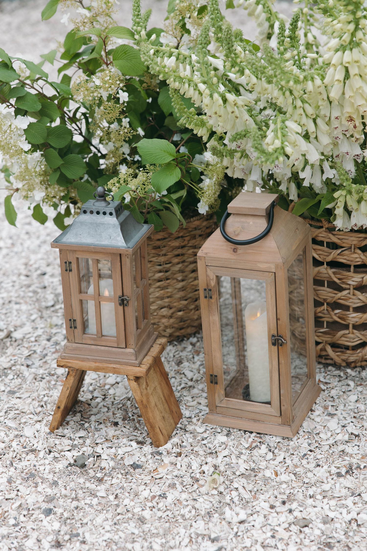 Wooden lanterns decorated with white flowers and greenery arranged on gravel surface.