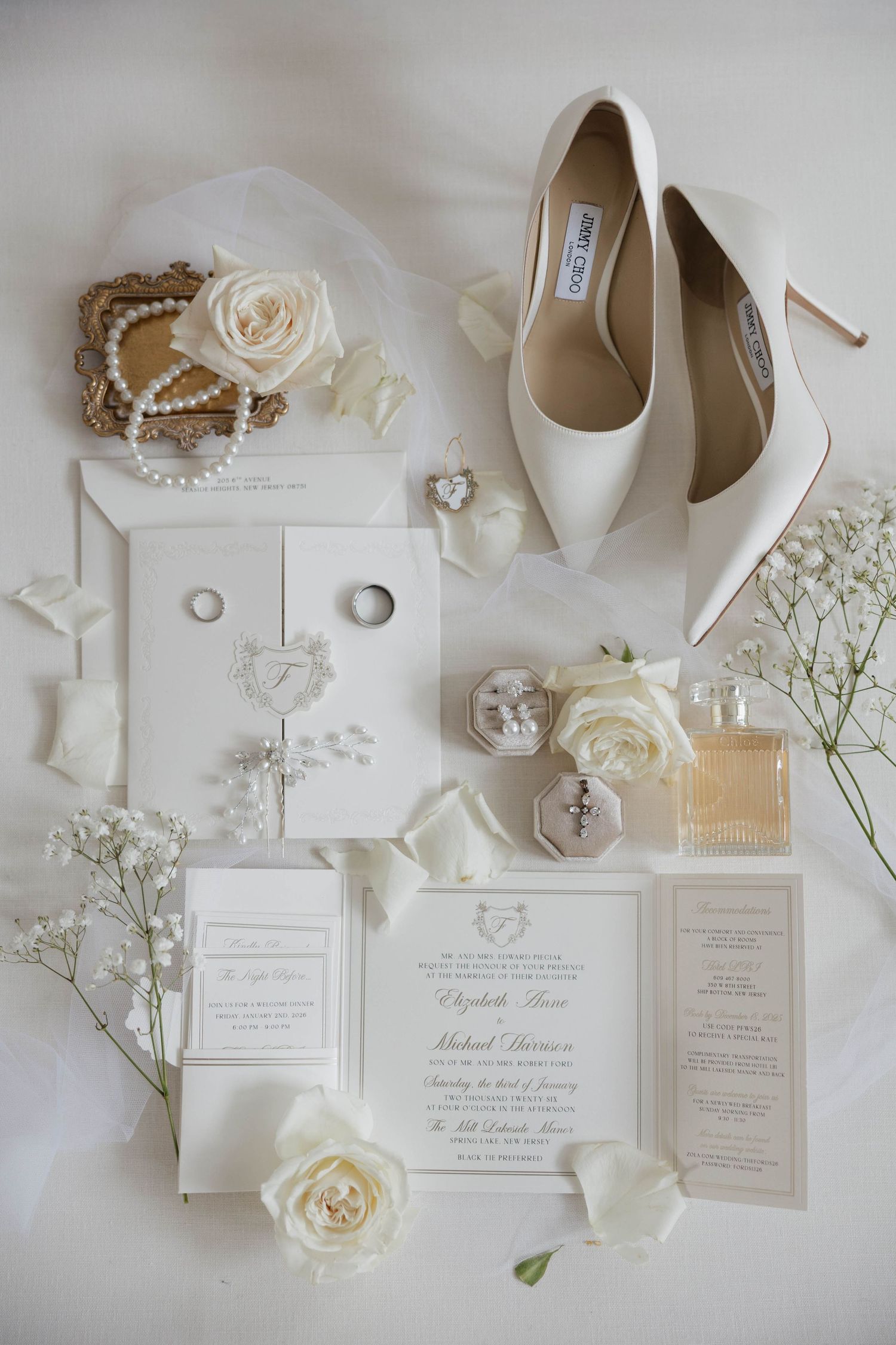 Elegant wedding details in white featuring invitations, heels, roses and pearls on light background.