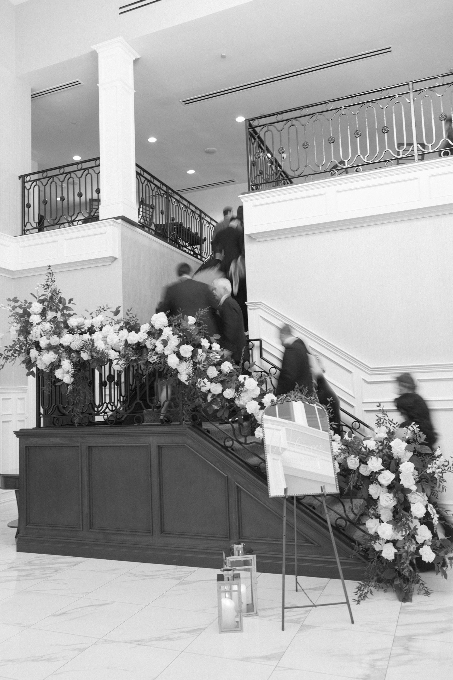 Elegant staircase adorned with white floral arrangements and lanterns in black and white.