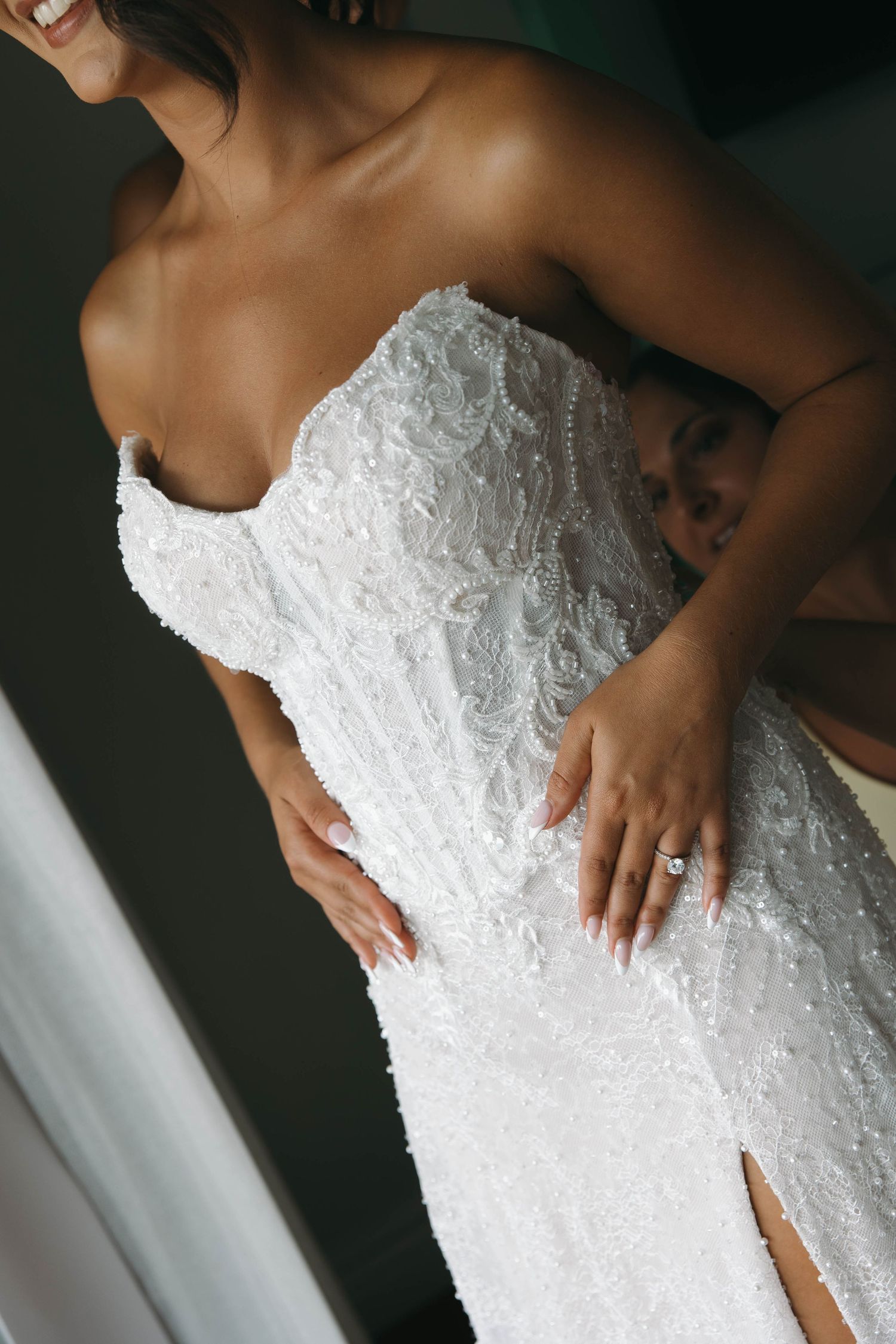 Close-up of bride in strapless beaded lace wedding dress with diamond engagement ring on her hand.