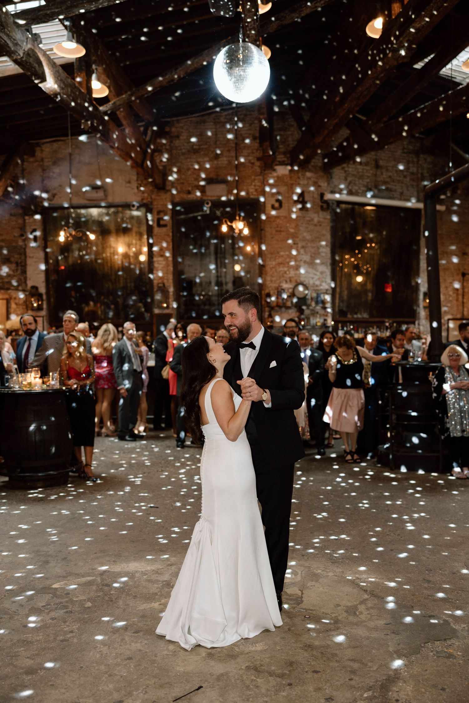First dance at wedding reception with confetti falling in a dimly lit venue.