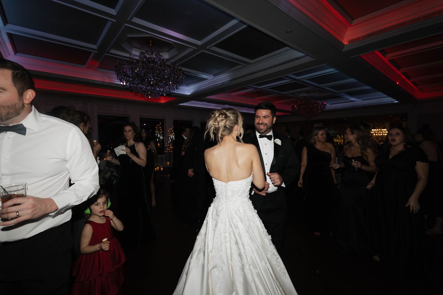 Wedding reception dance floor with dramatic red lighting and guests in silhouette.