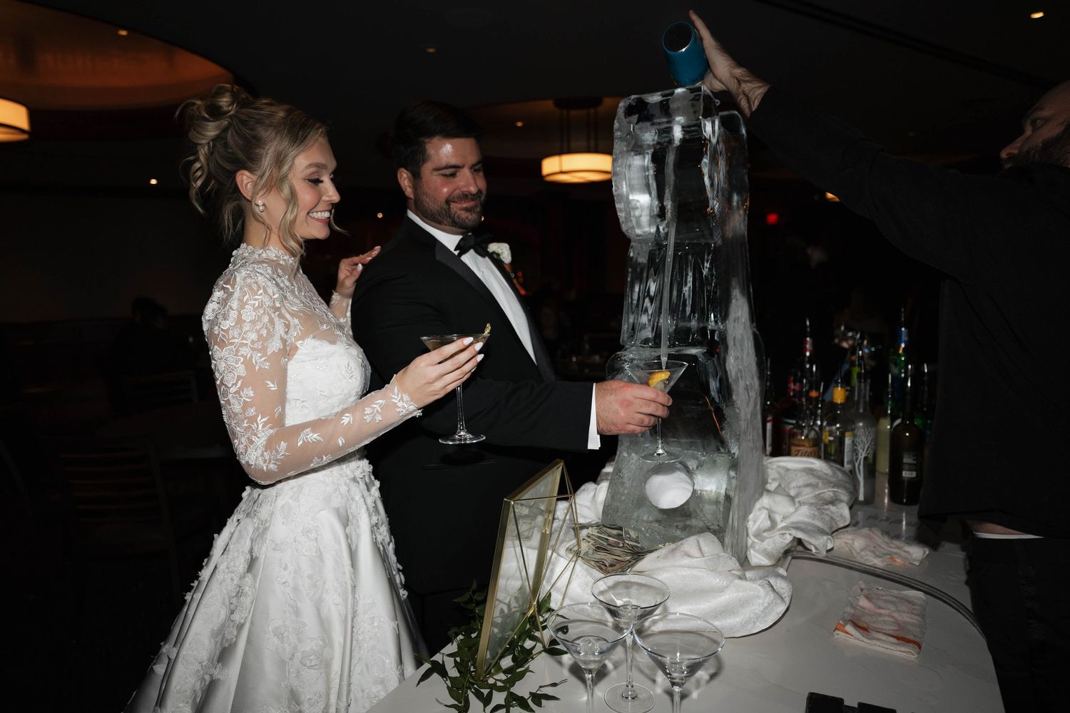 Wedding reception table setting with glassware and decorative elements in dim lighting.