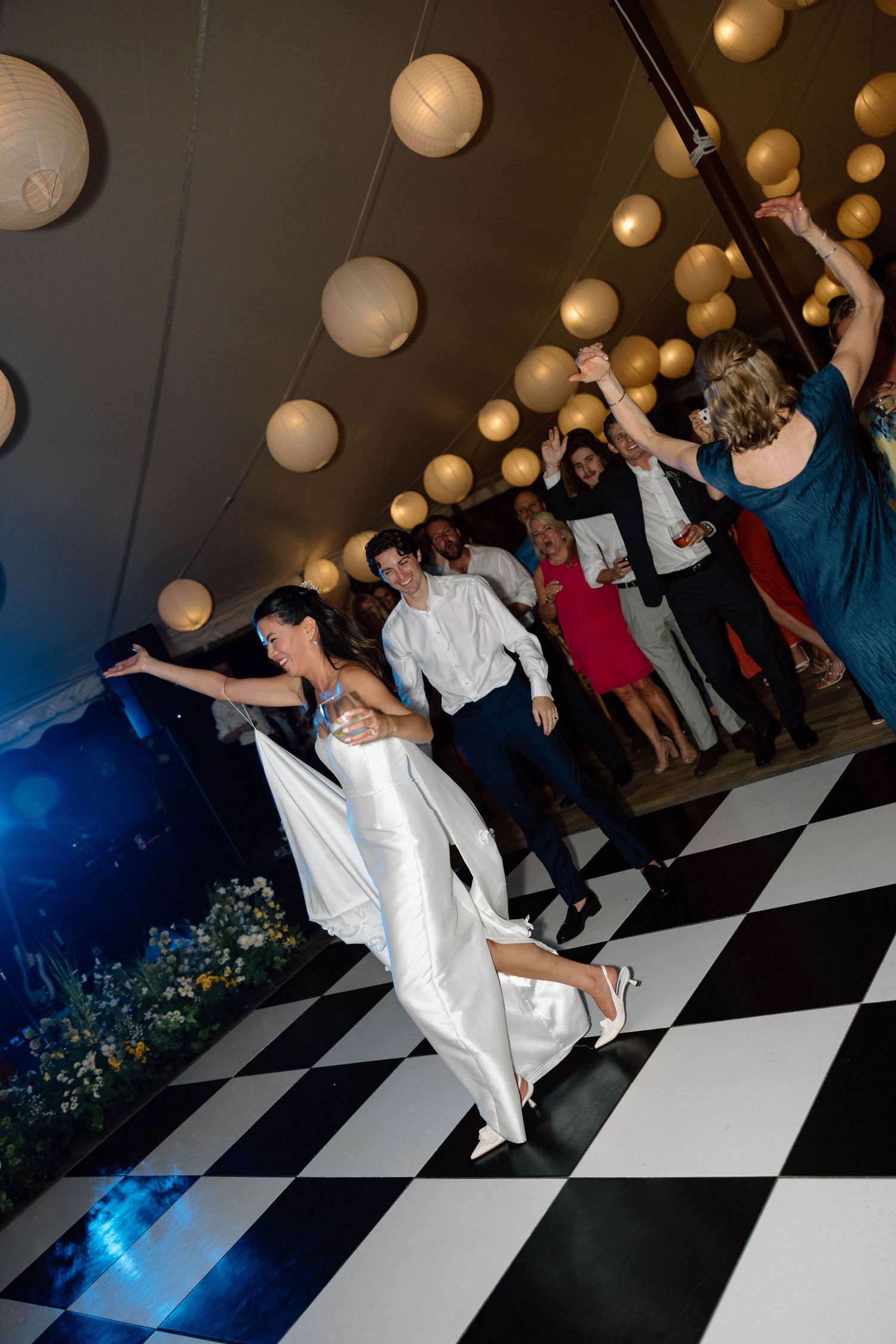 Wedding reception dance floor with black and white checkered pattern and hanging lanterns.
