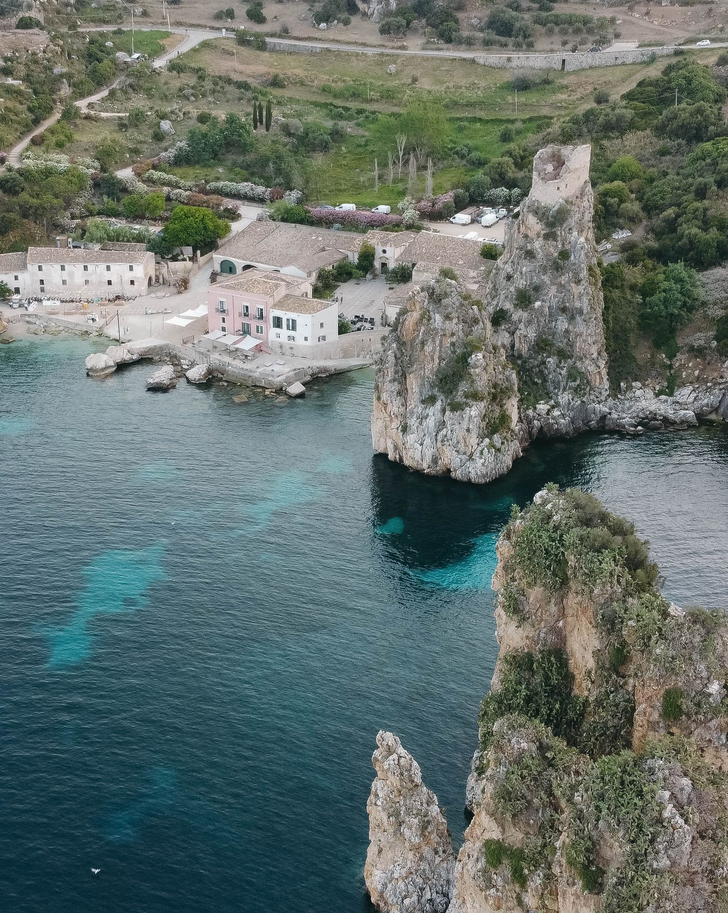 Drone view of a picturesque coastal inlet with traditional architecture and dramatic rock formations.