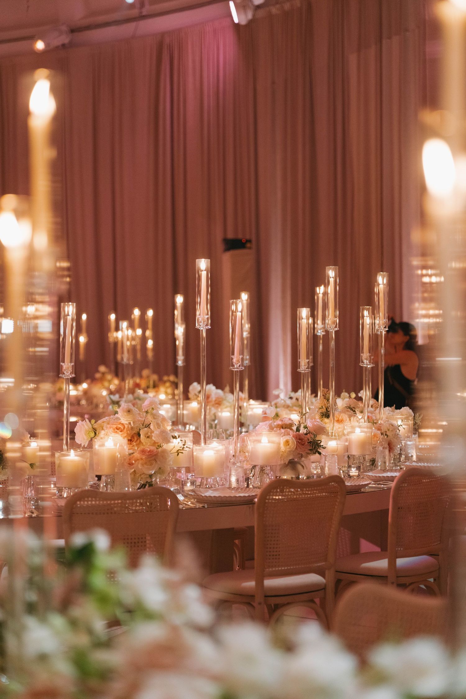 Long banquet tables set with crystal candelabras and white floral arrangements in a softly lit reception space.