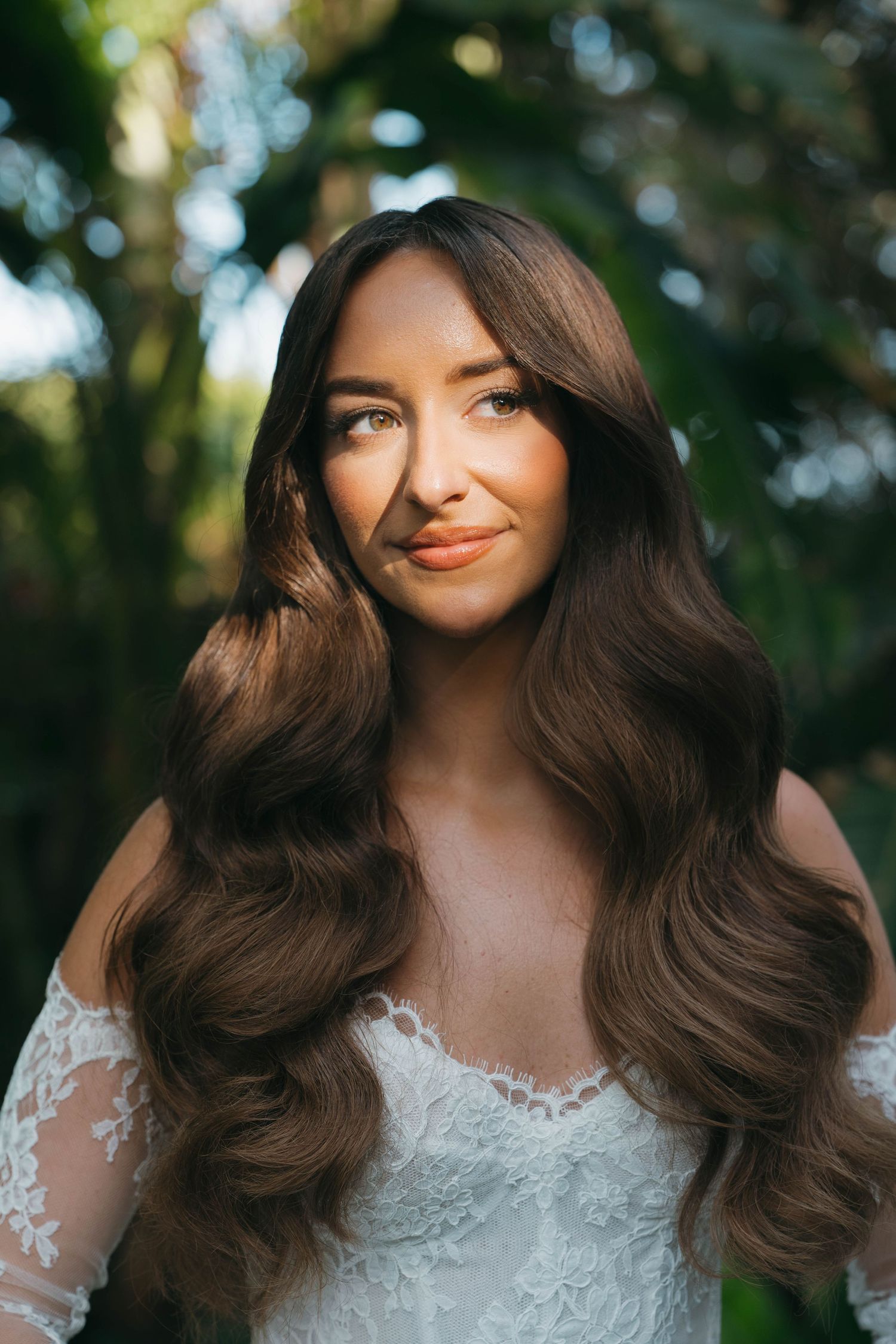 Close-up portrait of bride with flowing dark hair and lace wedding dress in natural lighting.