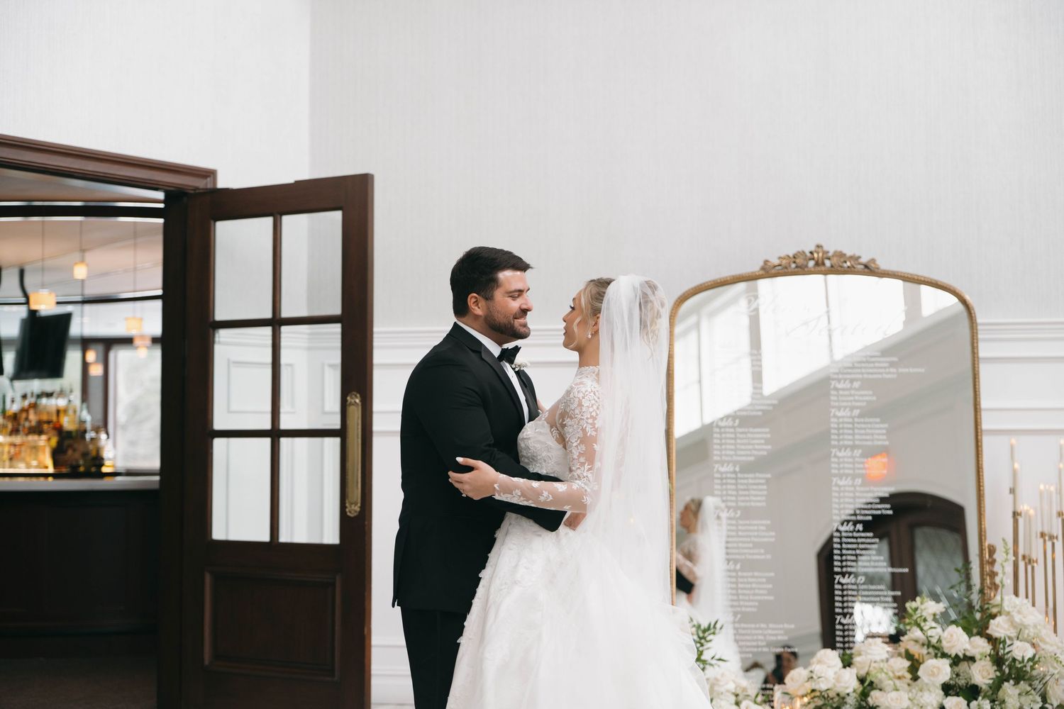 Elegant wedding venue interior with white walls and tall windows decorated with floral arrangements.
