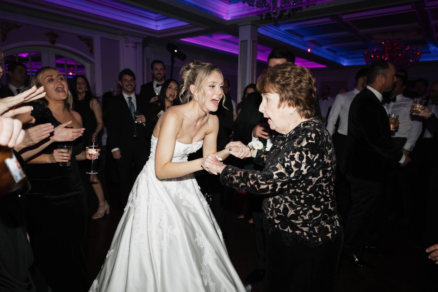 Lively dance floor scene at wedding reception with purple lighting effects.