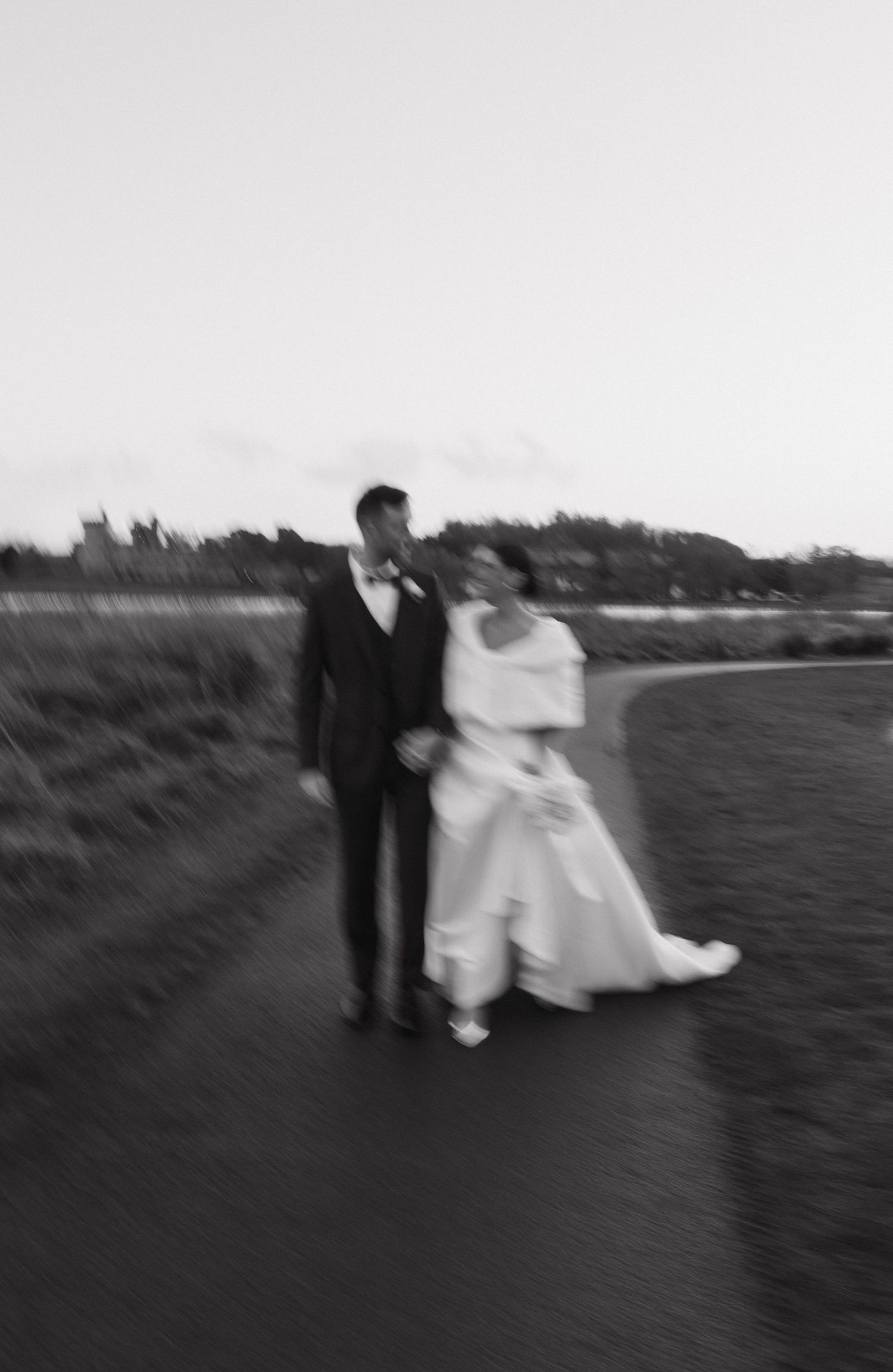 Blurred motion sequence of wedding couple walking along shoreline in black and white.