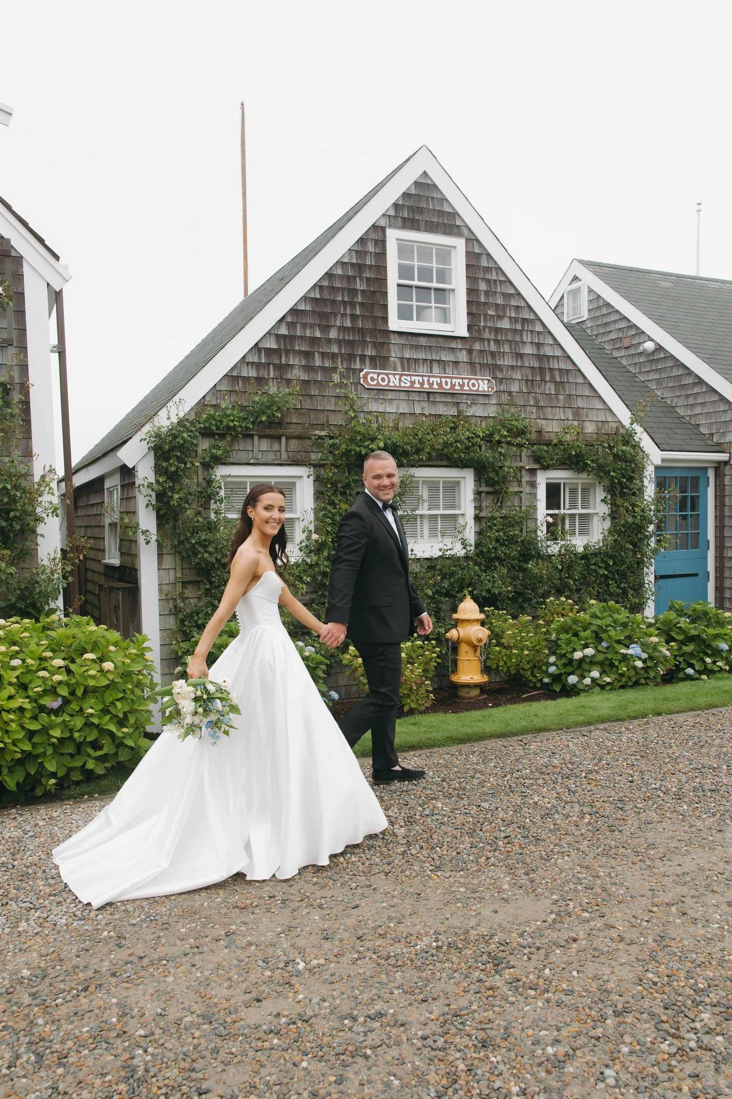 Wedding couple posing outside a charming Cape Cod style cottage with hydrangea bushes.