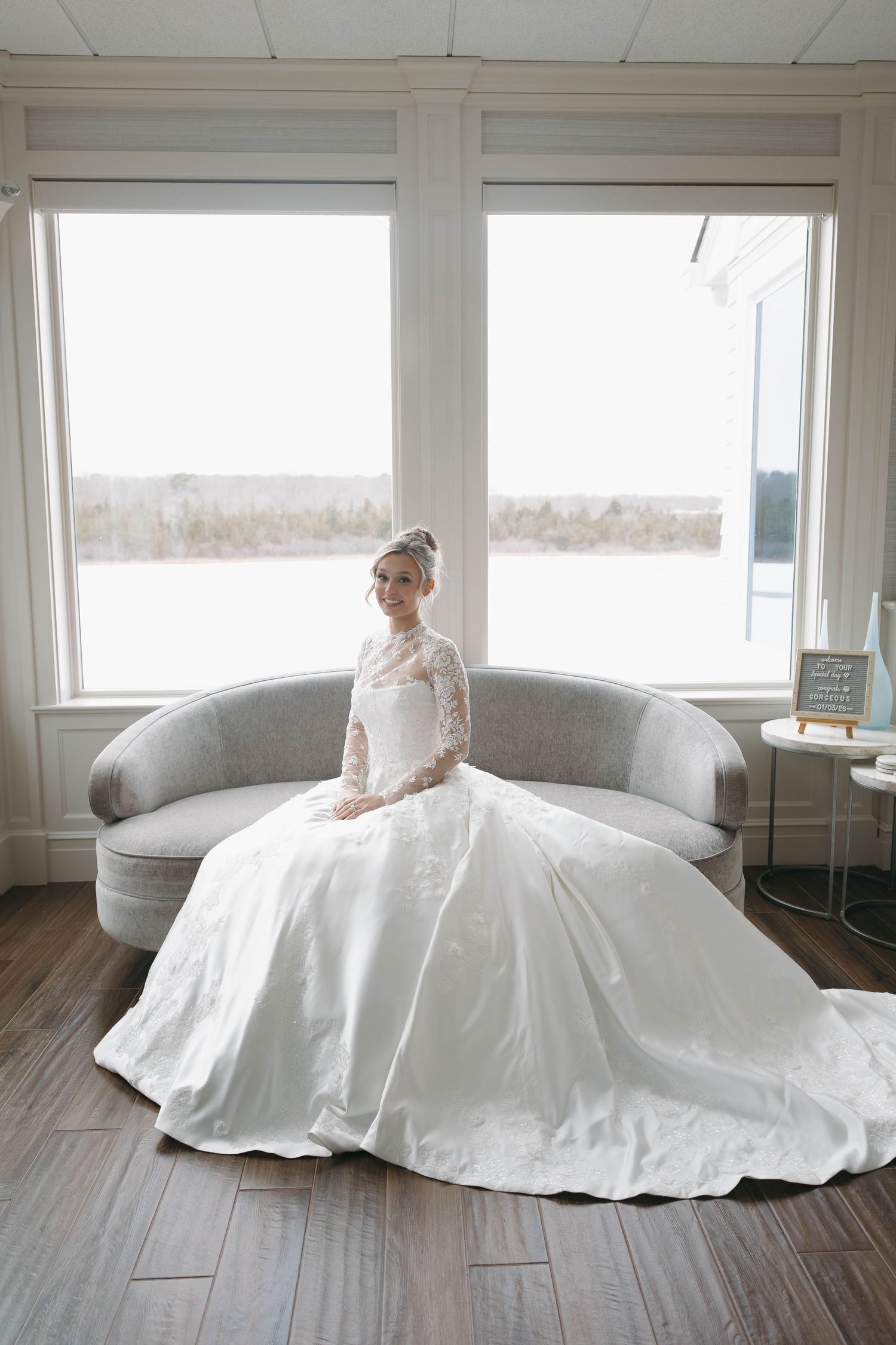 Bride seated on curved sofa in elegant lace and satin wedding gown.