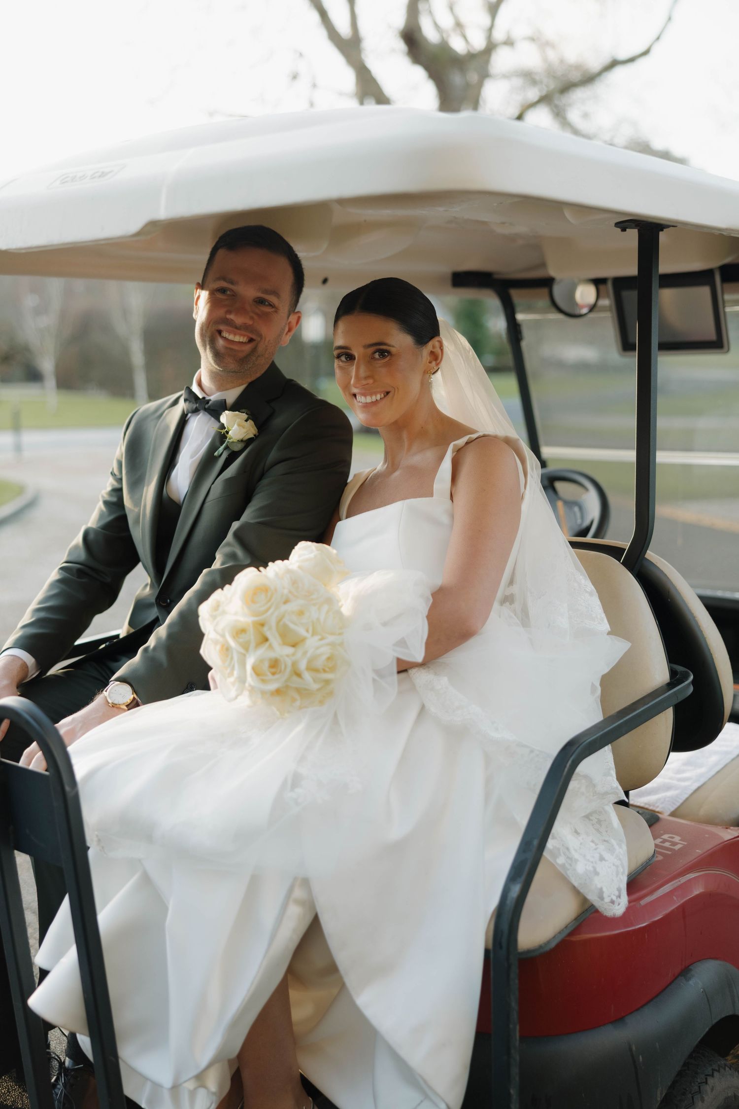 Newlyweds sit together in vintage golf cart at wedding venue.