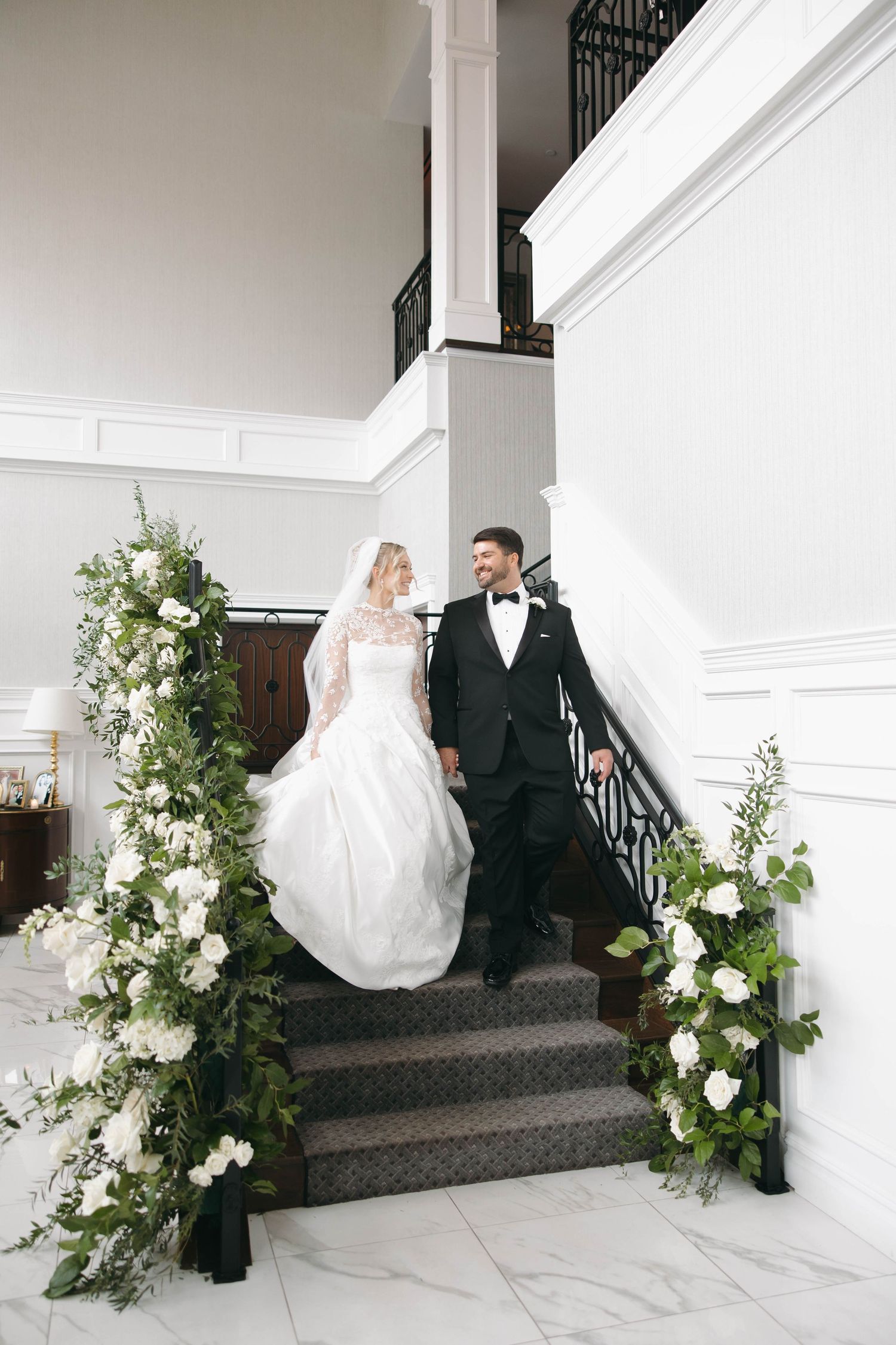 Wedding couple poses on elegant staircase decorated with white floral arrangements.