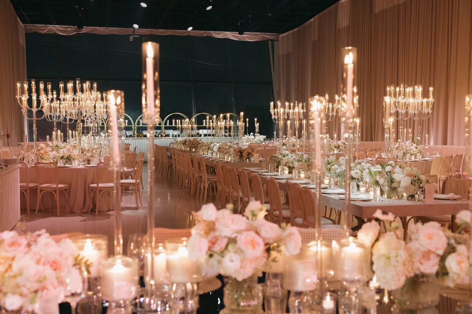 Wedding reception venue with pink and white decor, crystal lighting, and elegant table settings.