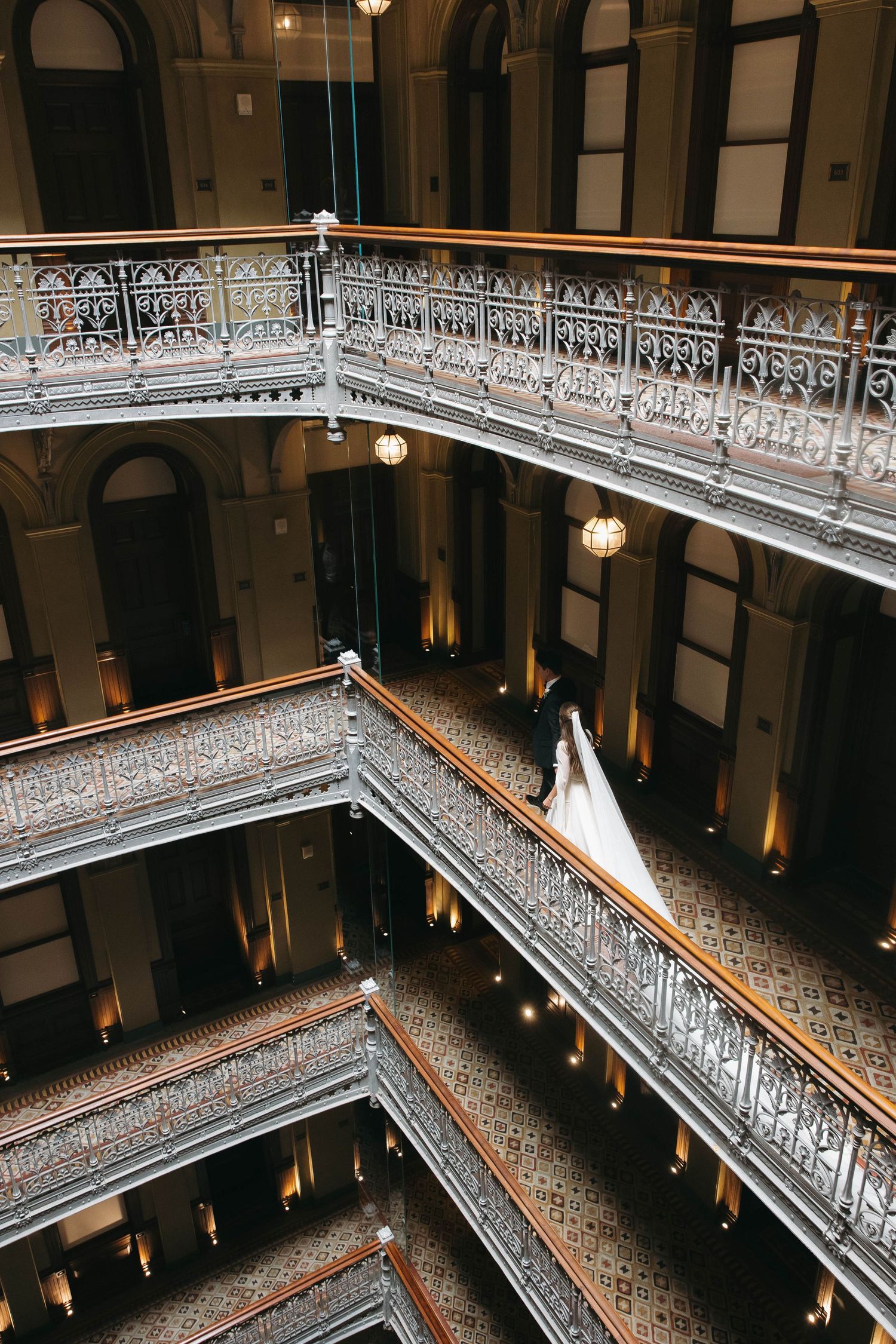 Bride in white gown standing on ornate multi-level balcony of elegant historic building with decorative railings.