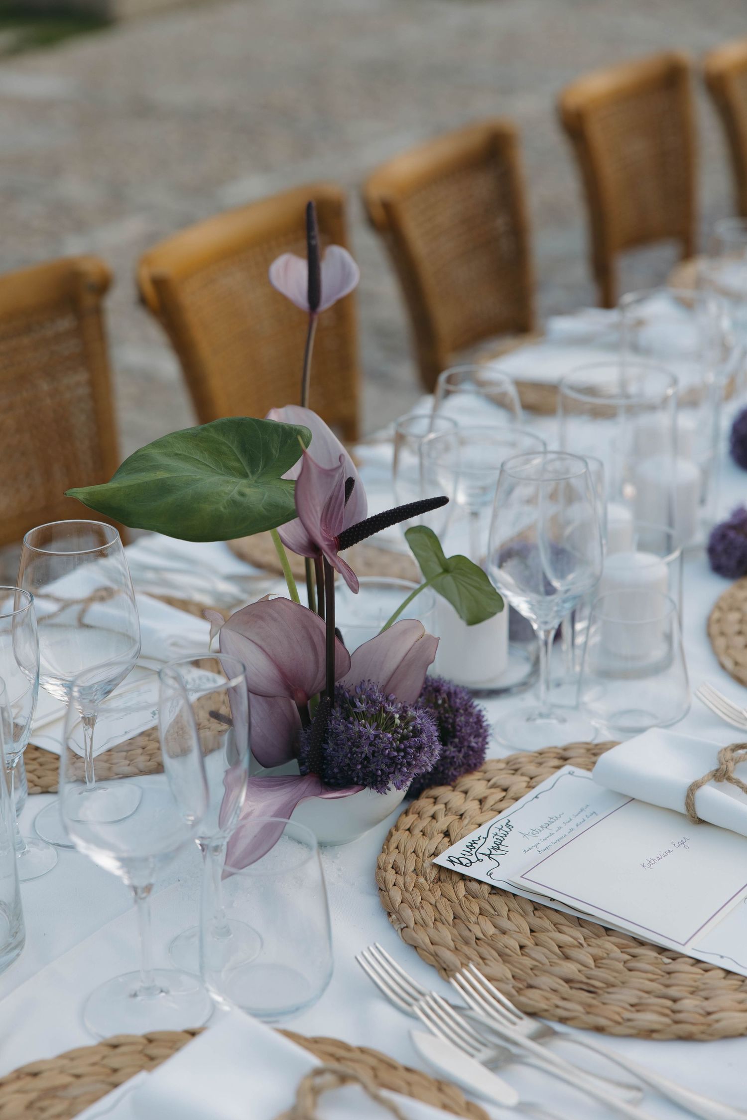 Elegant place settings with woven placemats, glassware, and purple floral decorations.