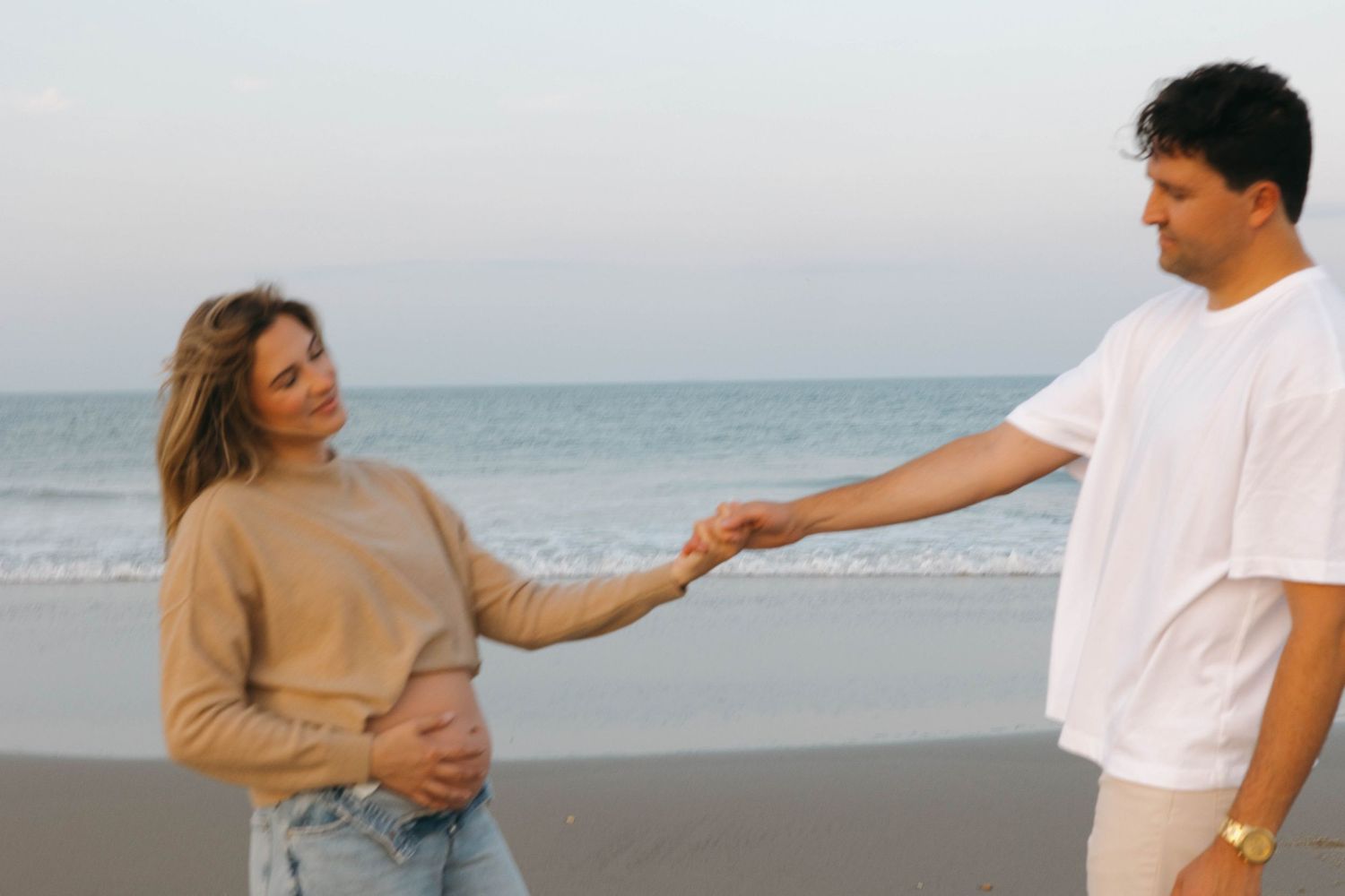 A couple walks hand in hand along a scenic beach at sunset with ocean waves in the background.