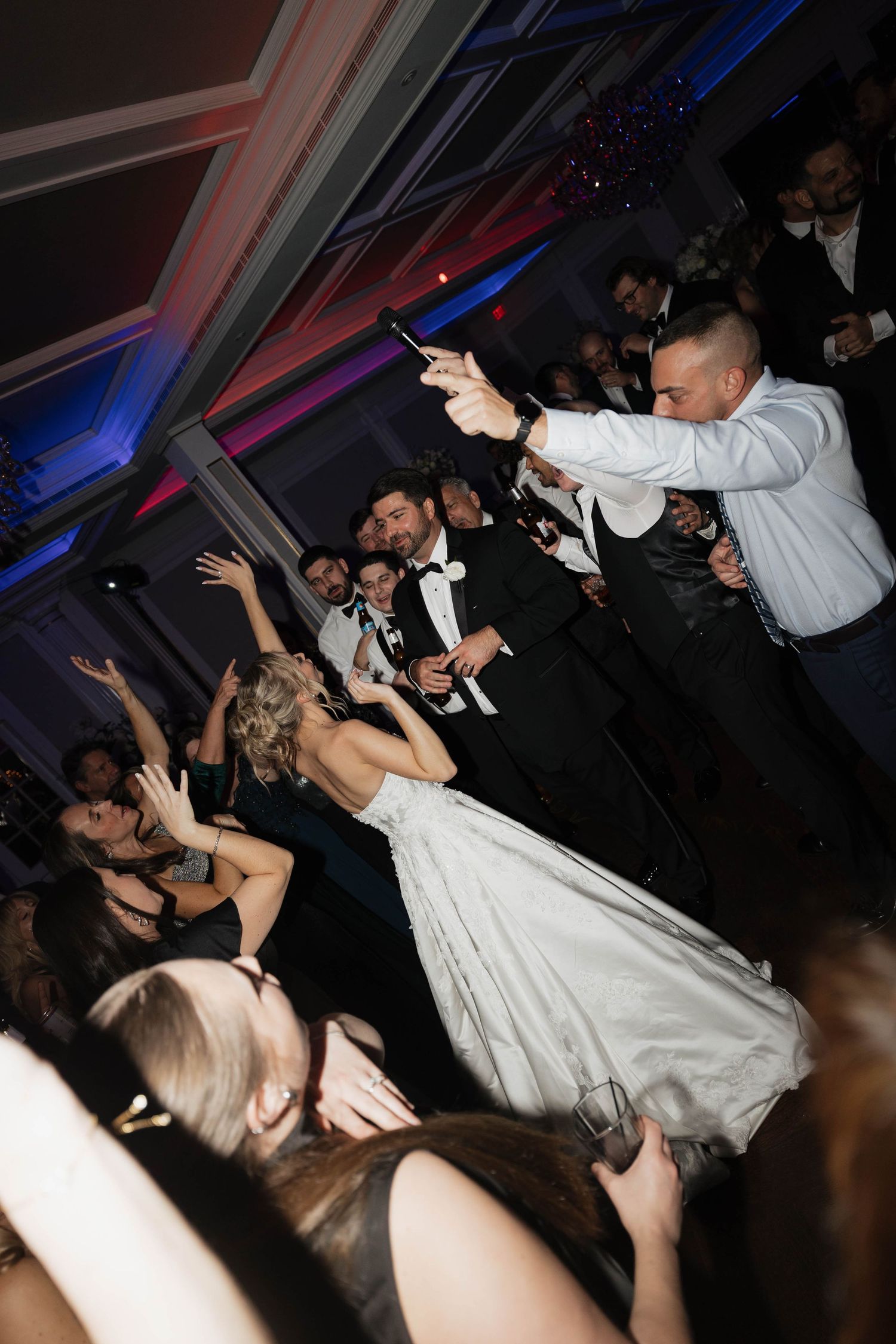 Bride in white gown dances surrounded by guests during wedding reception.