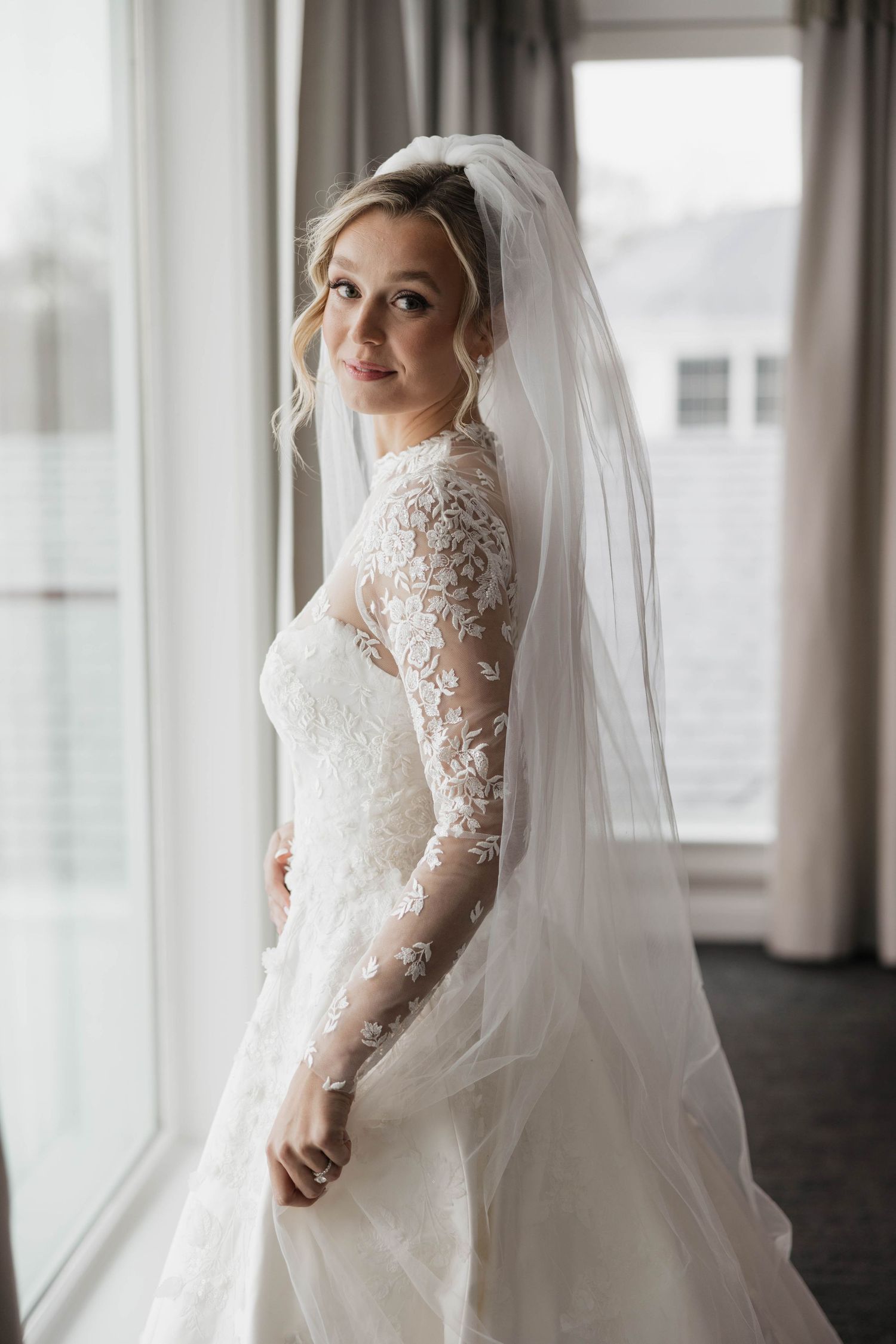 Wedding gown with intricate lace details and long sleeves photographed by bright windows.