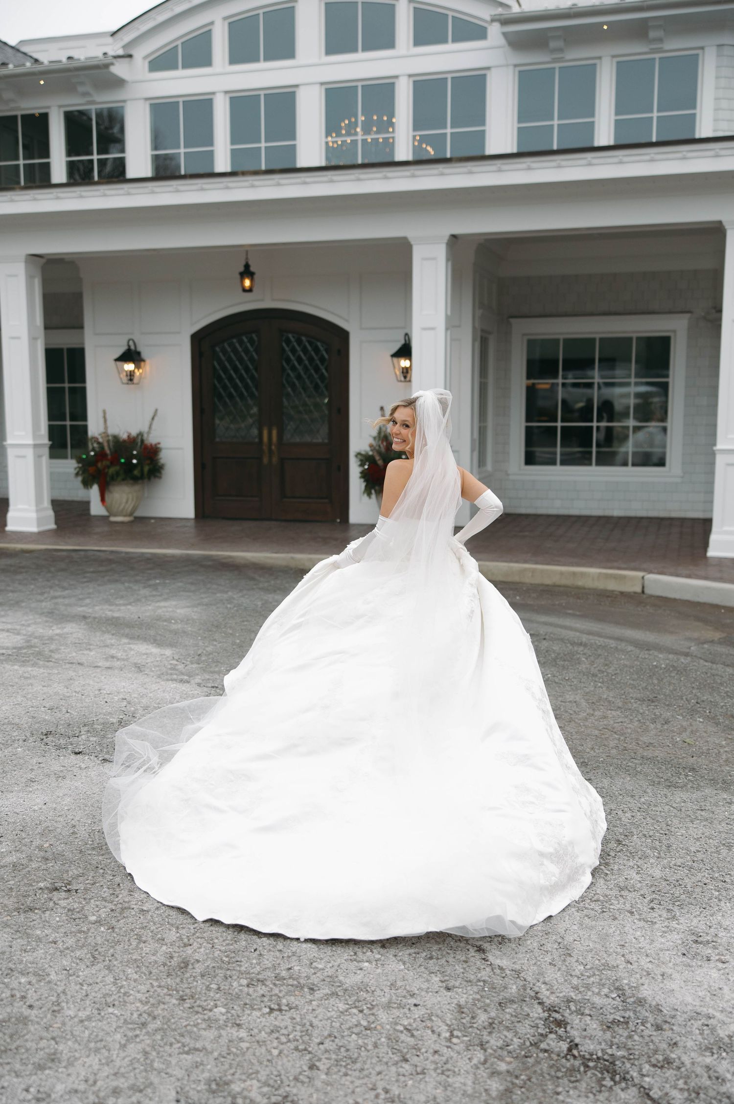 A stunning bridal gown with cathedral train spreads across the ground in front of a white building.
