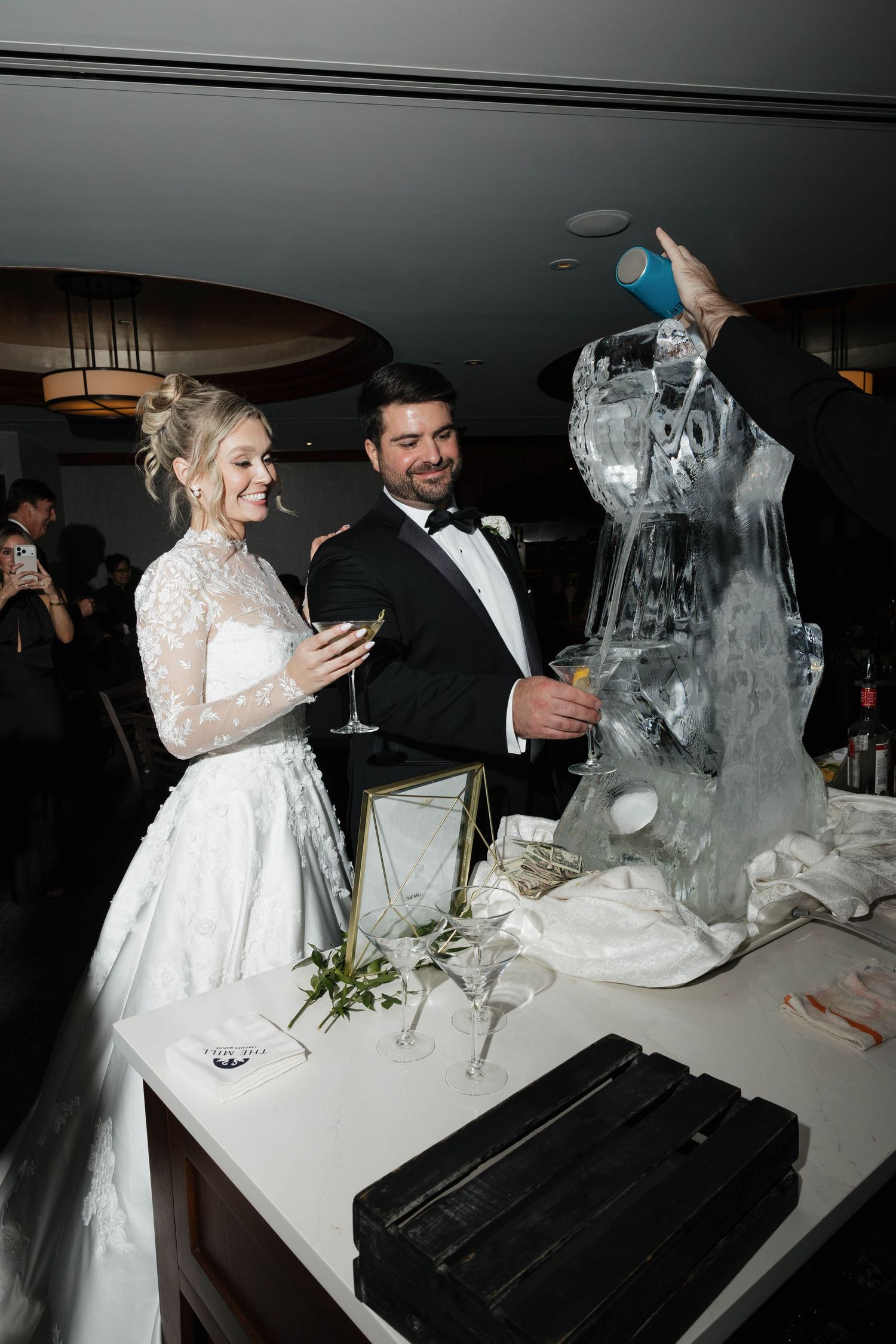A couple in wedding attire admires an elaborate ice sculpture at their reception.