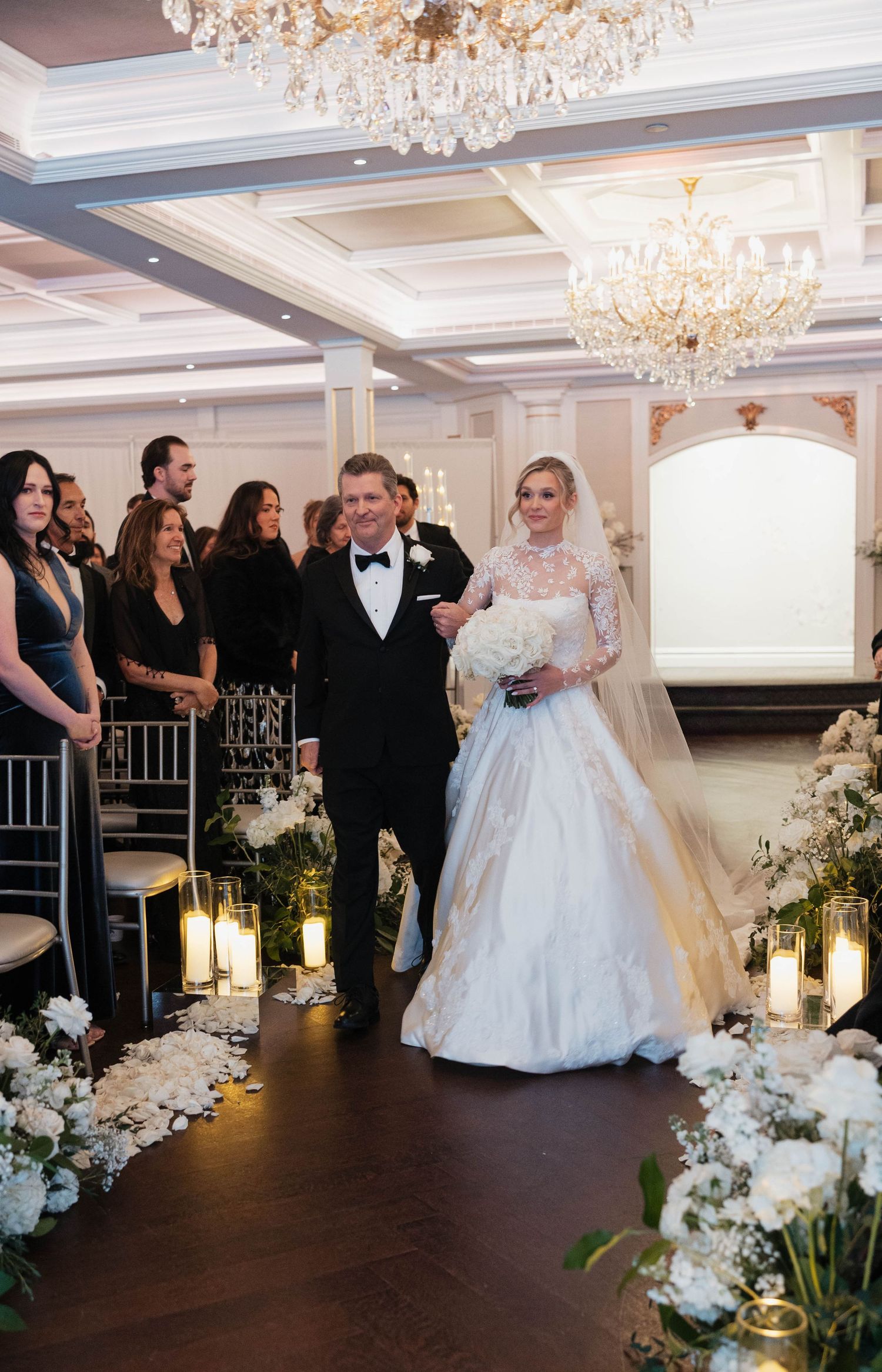 Wedding celebration in an opulent ballroom decorated with white flowers and crystal lighting.