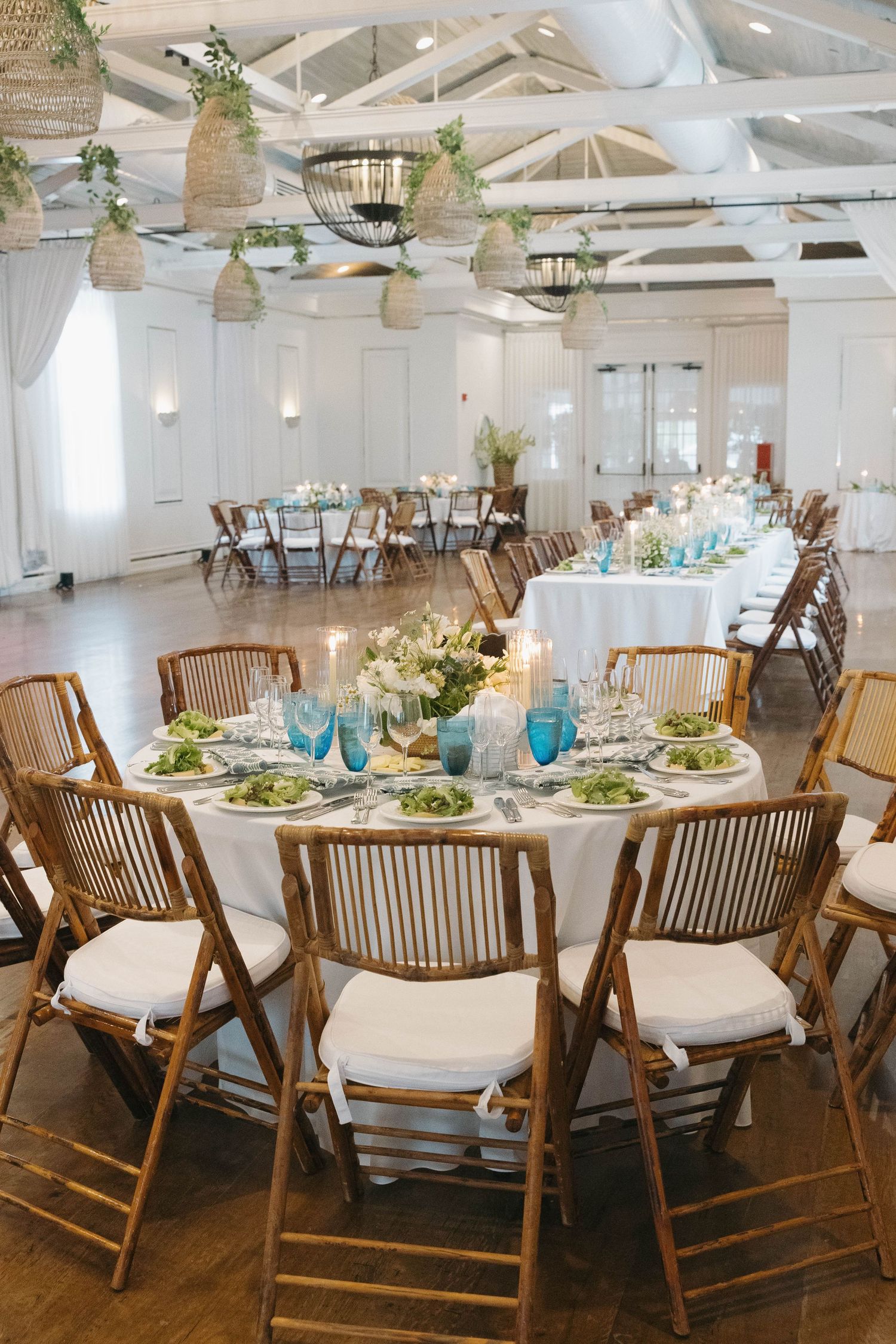Long banquet tables with wooden chairs and white linens set up in a bright reception hall.