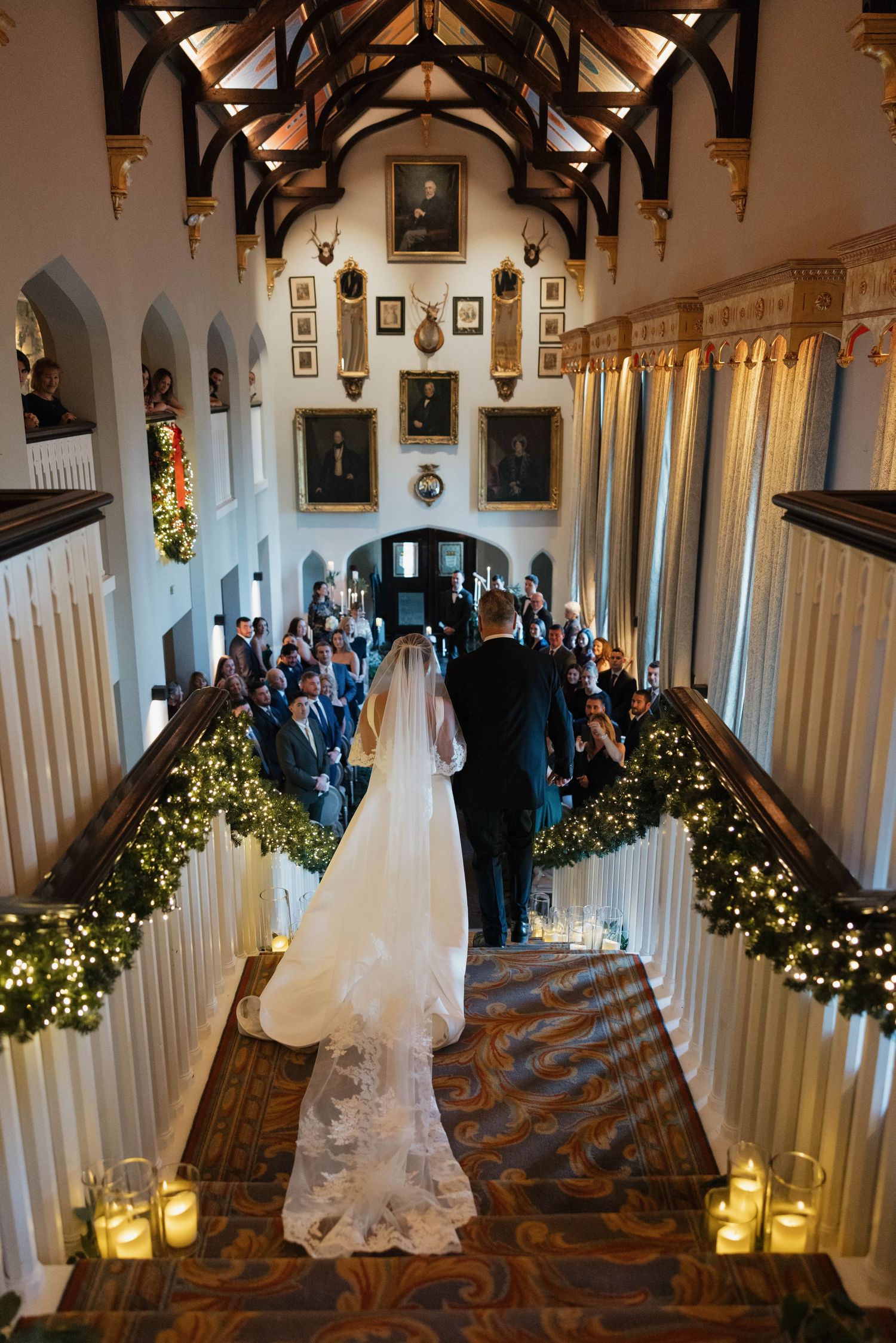 An elegant castle hallway decorated with twinkling lights and greenery for a wedding ceremony.