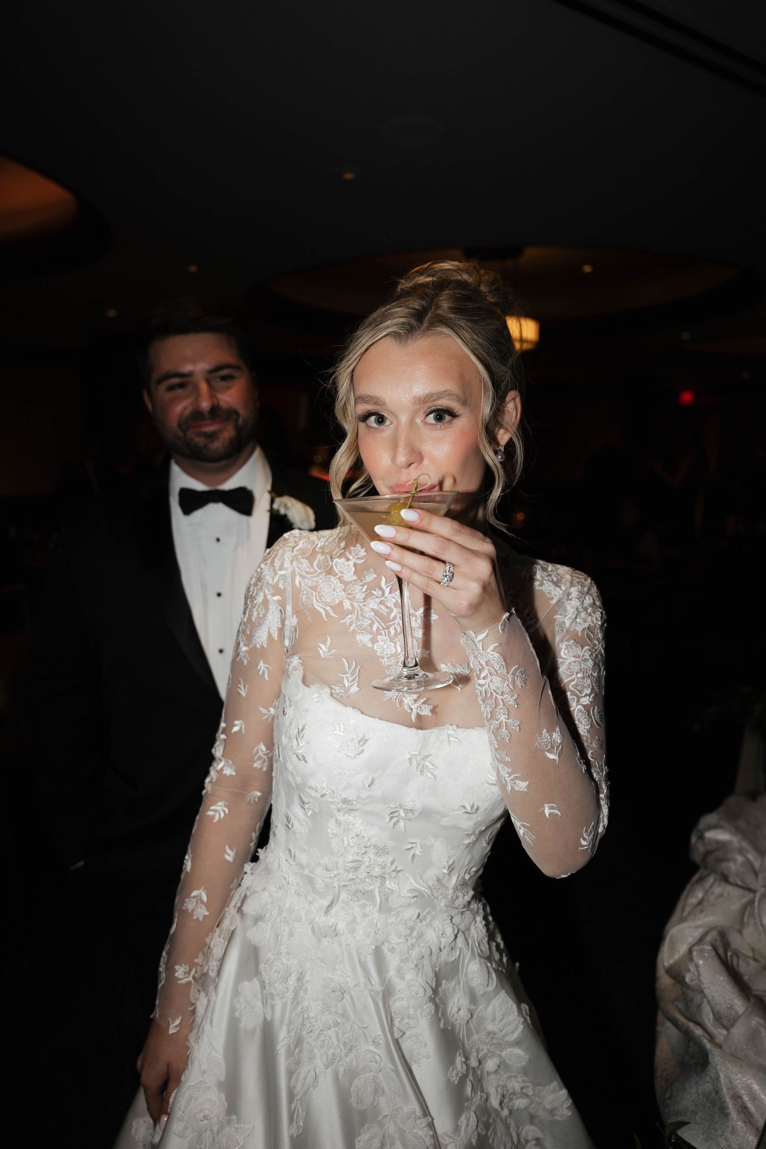 Bride in lace-detailed dress enjoys a celebratory drink at wedding reception.